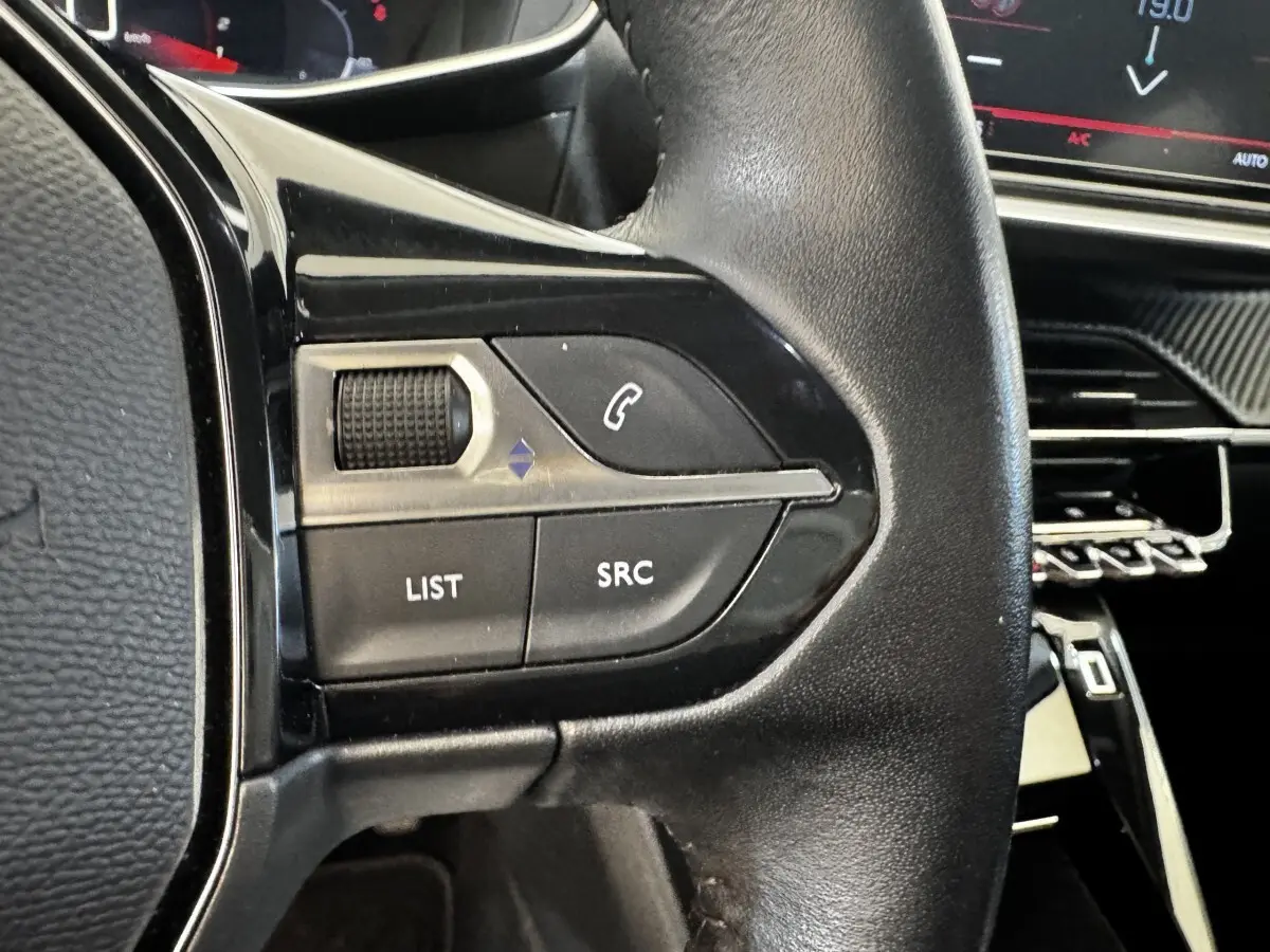 Gros plan sur le volant cuir noir multifonctions de la Peugeot 2008 blanc, avec commandes audio et téléphone intégrées.