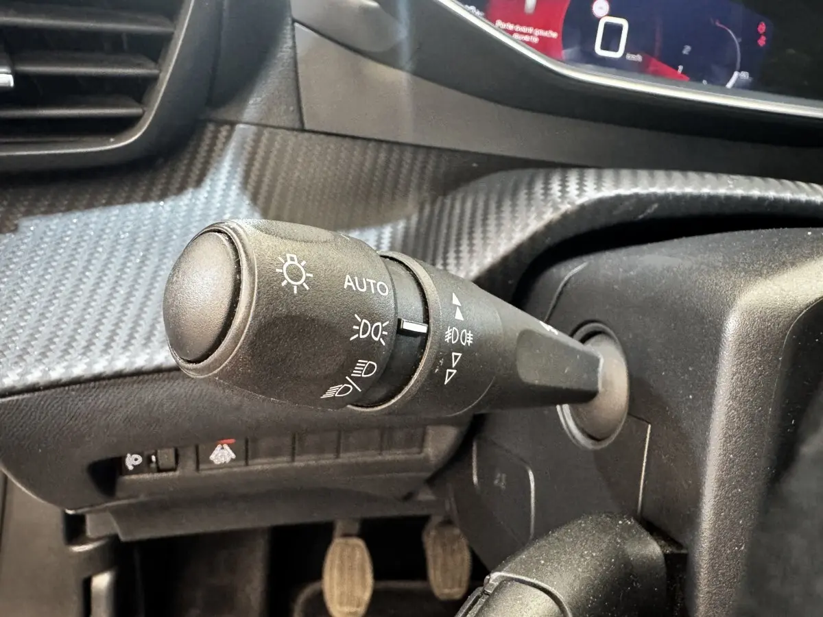 Gros plan sur la commande des feux avec réglage automatique dans l’habitacle noir du Peugeot 2008 blanc, version Allure Business.