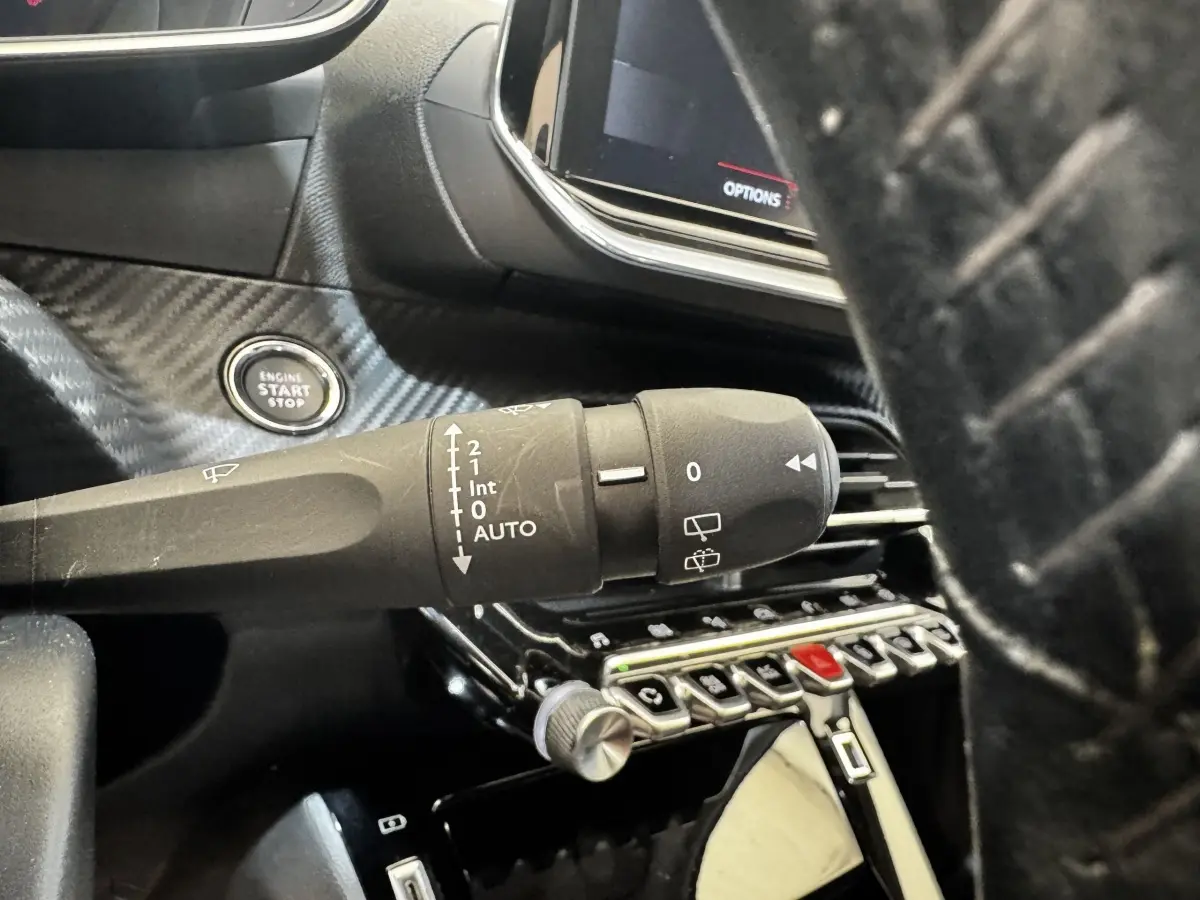 Gros plan sur la manette d'essuie-glace et le bouton start/stop du tableau de bord noir du Peugeot 2008 blanc, version Allure Business.