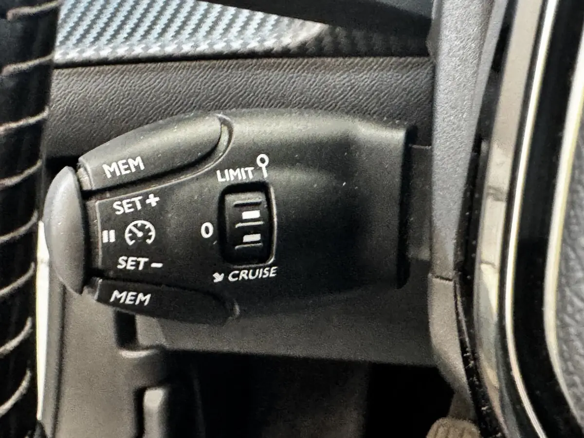 Gros plan sur la commande de régulateur de vitesse noire à gauche du volant dans l’habitacle d’un Peugeot 2008 blanc.