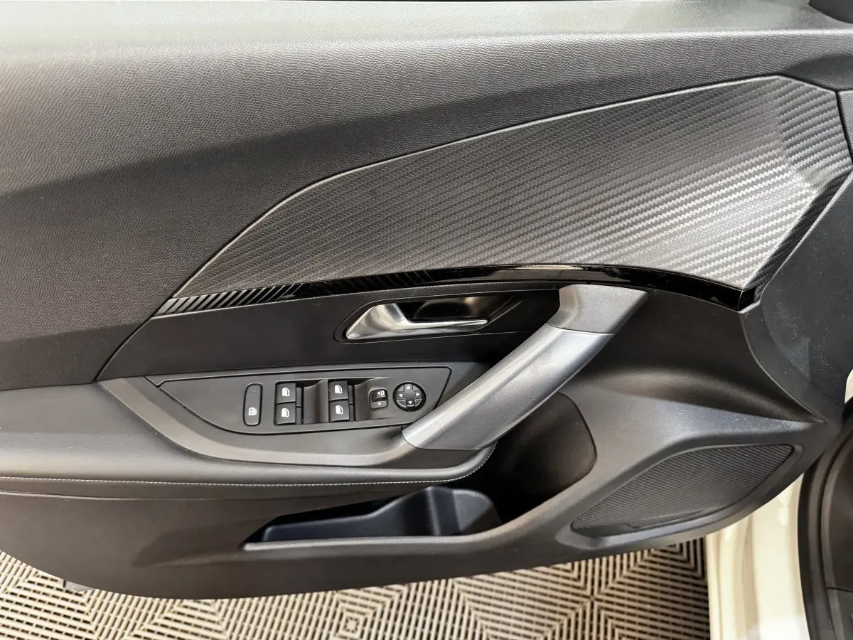 Vue rapprochée de la porte avant gauche blanche du Peugeot 2008 avec commandes électriques et insert décoratif carbone.