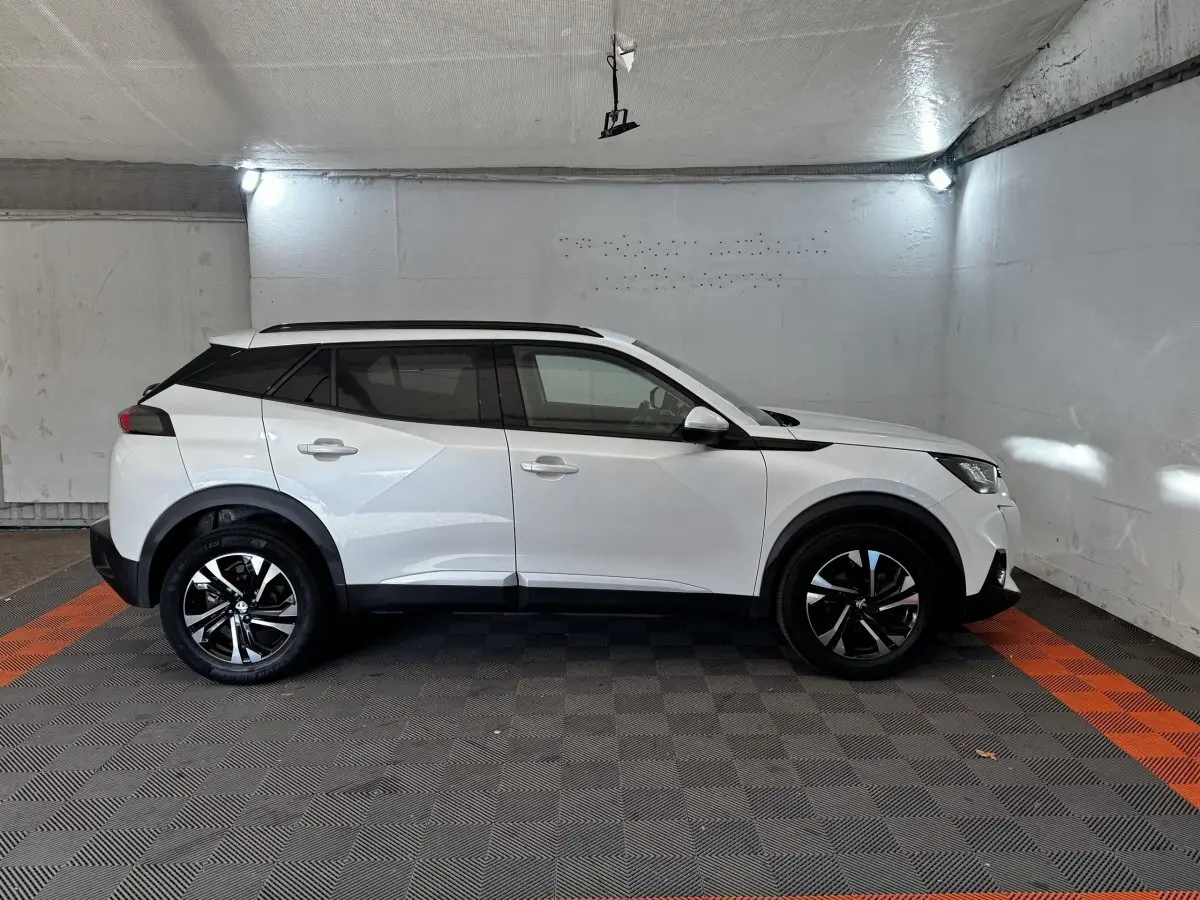 Peugeot 2008 blanc vue de profil côté gauche dans un garage, avec jantes noires et toit noir contrastant.