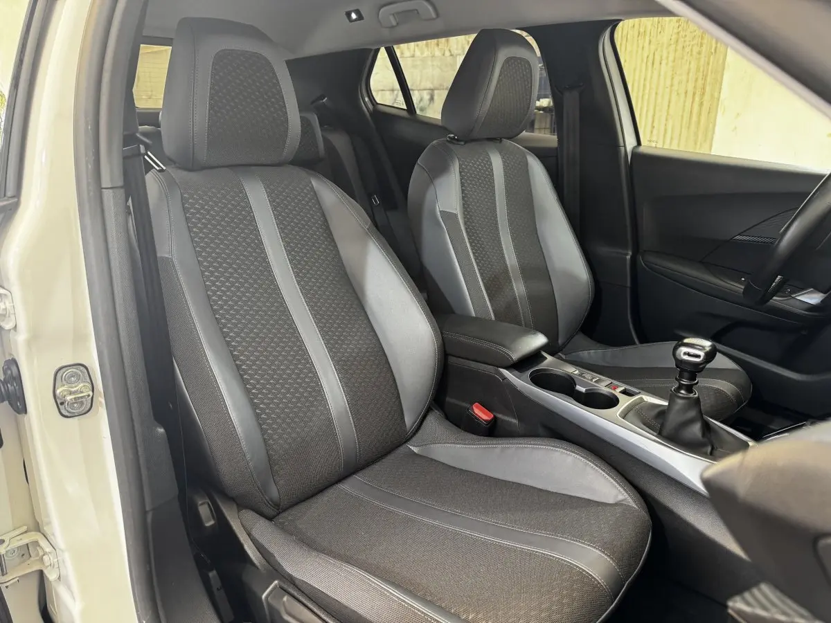 Vue intérieure côté avant gauche du Peugeot 2008 blanc, mettant en valeur les sièges tissu et cuir et la boîte manuelle.