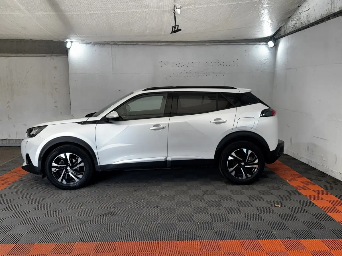 Peugeot 2008 blanc vue de profil côté gauche, avec toit noir et jantes alliage bicolores dans un garage.
