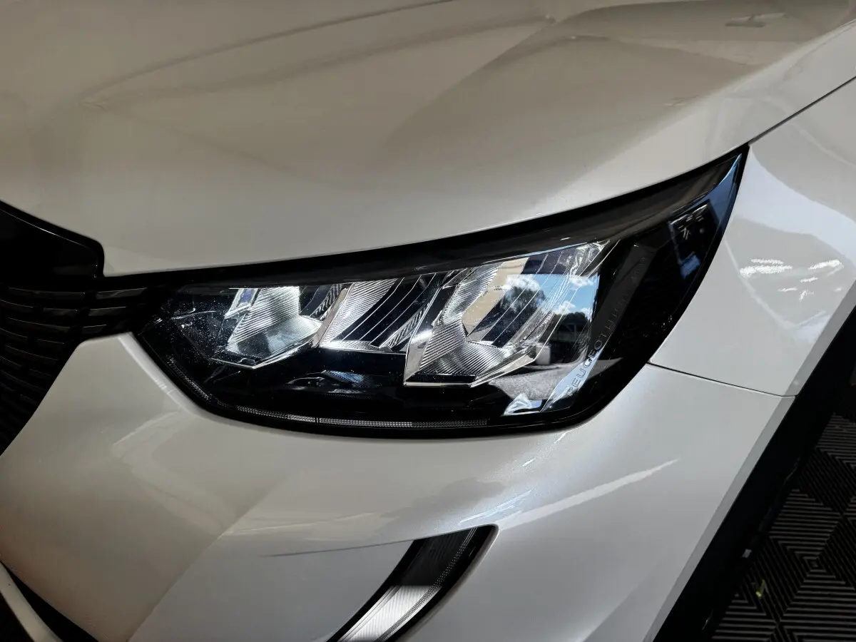 Gros plan sur le phare avant droit blanc du Peugeot 2008, mettant en valeur le design moderne et les détails lumineux.