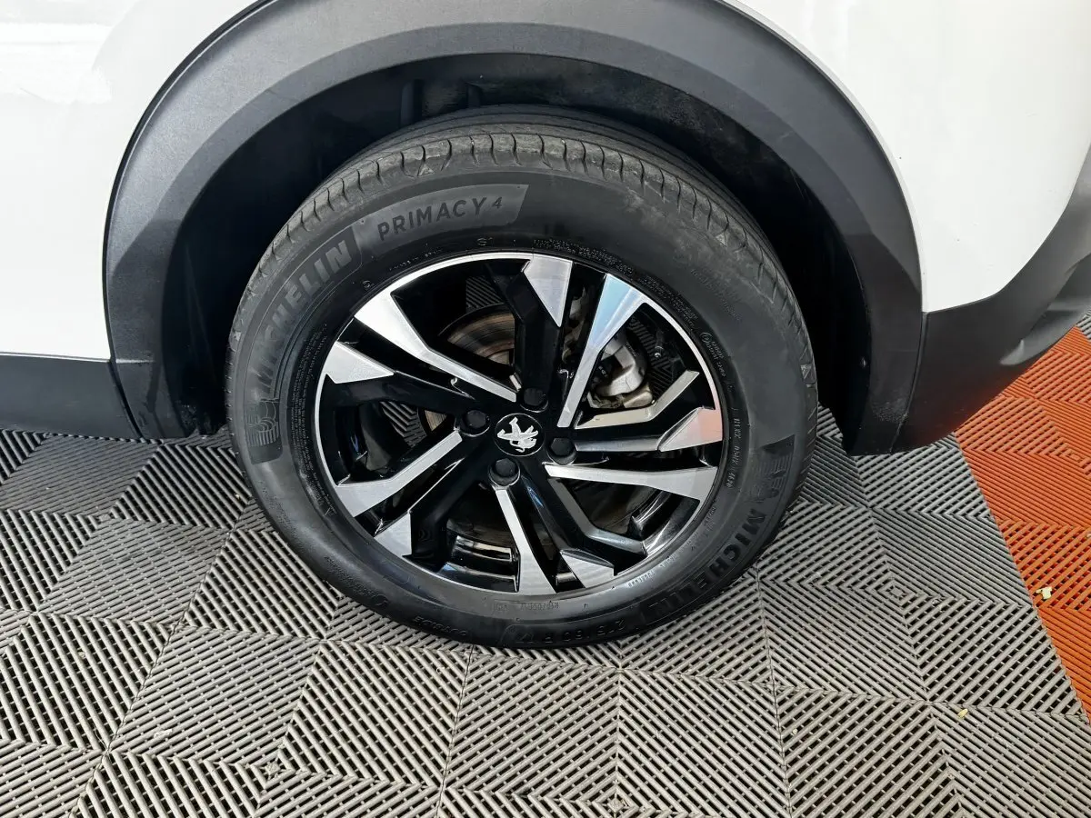Gros plan sur la roue arrière droite d’un Peugeot 2008 blanc avec jante alliage noire et argentée.