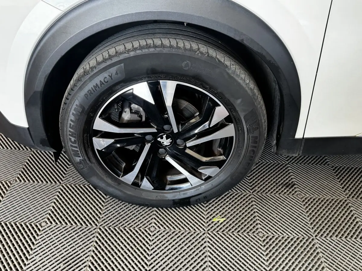 Gros plan sur la roue avant gauche noire et argentée du Peugeot 2008 blanc, avec jante au design moderne.