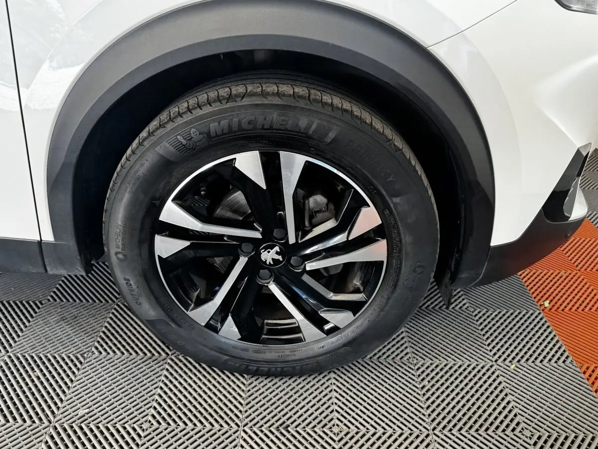 Gros plan sur la roue avant droite noire et argentée d'un Peugeot 2008 blanc avec partie de l'aile visible.