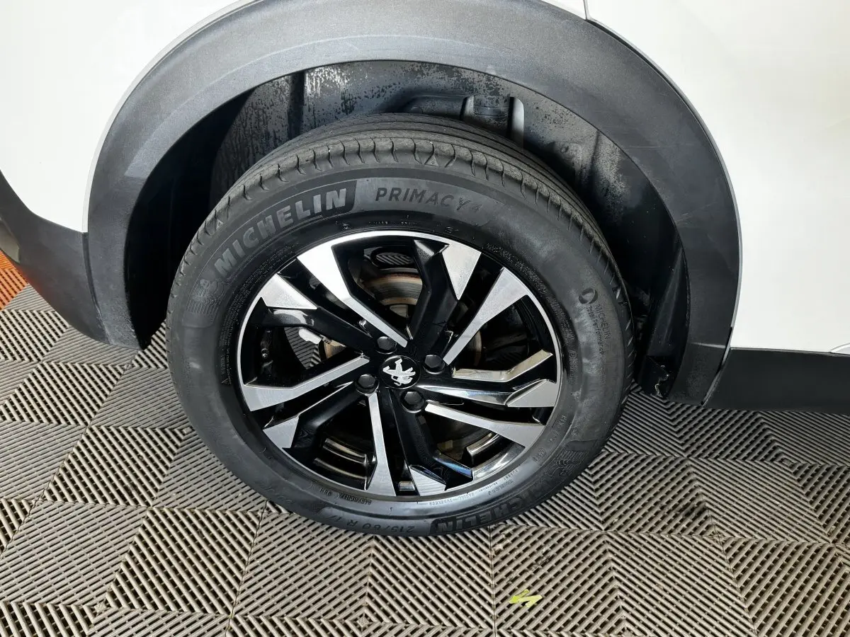 Gros plan sur la roue arrière droite d’un Peugeot 2008 blanc avec jante alliage noire et argentée.