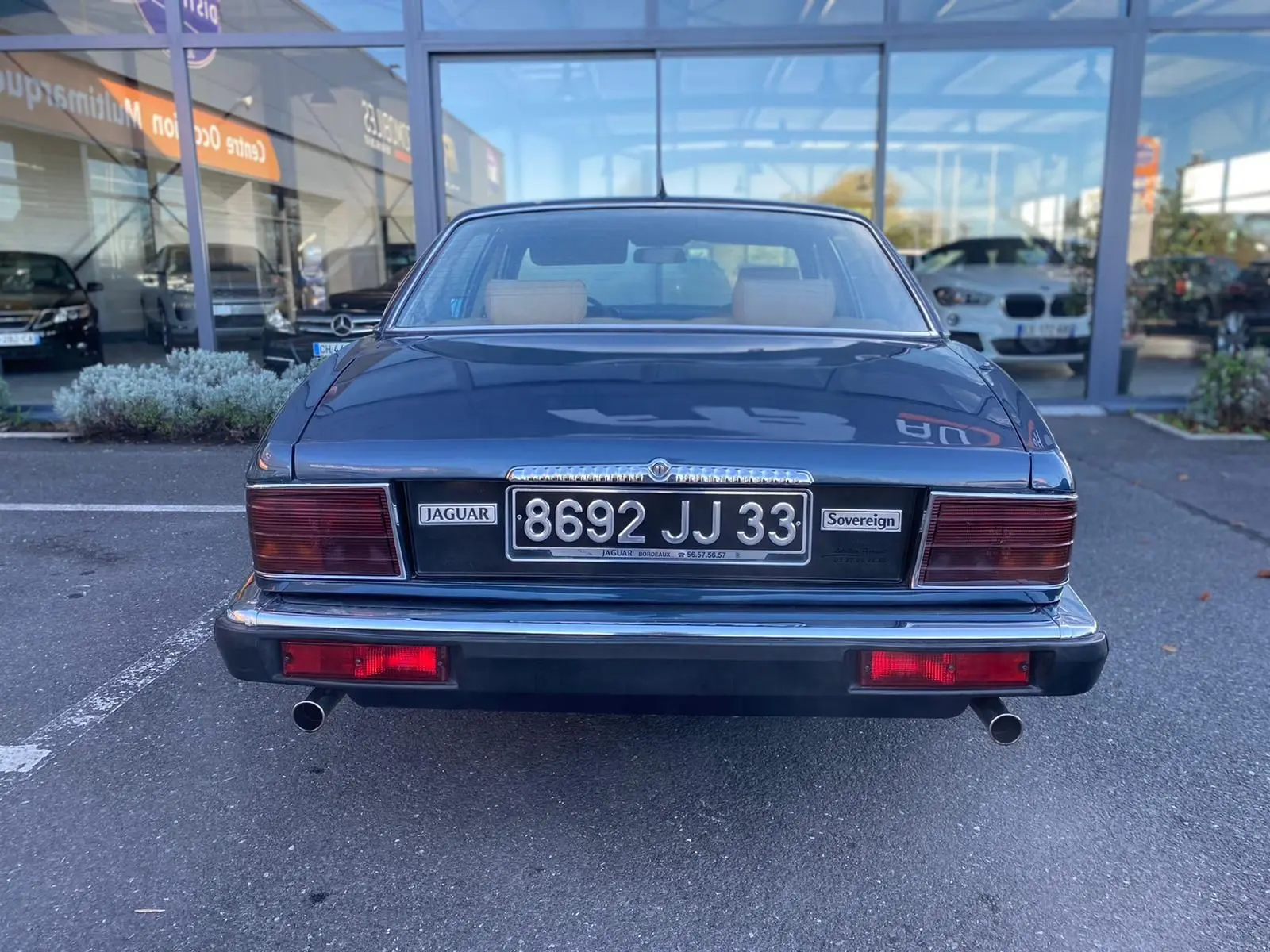 Vue arrière d'une Jaguar XJ6 3.6 Sovereign bleu de 1987 avec plaques et feux rouges rectangulaires visibles.
