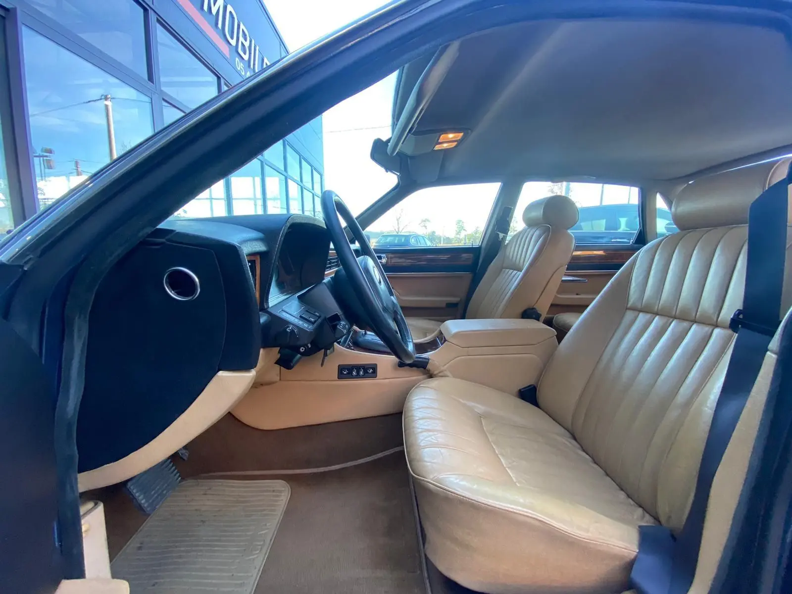 Intérieur beige de la Jaguar XJ6 3.6 Sovereign 1987, vue côté conducteur avec tableau de bord et sièges en cuir.