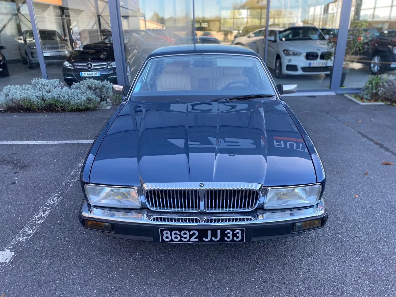 Jaguar XJ6 3.6 Sovereign bleu 1987 vue de face, avec calandre chromée et phares rectangulaires allumés.