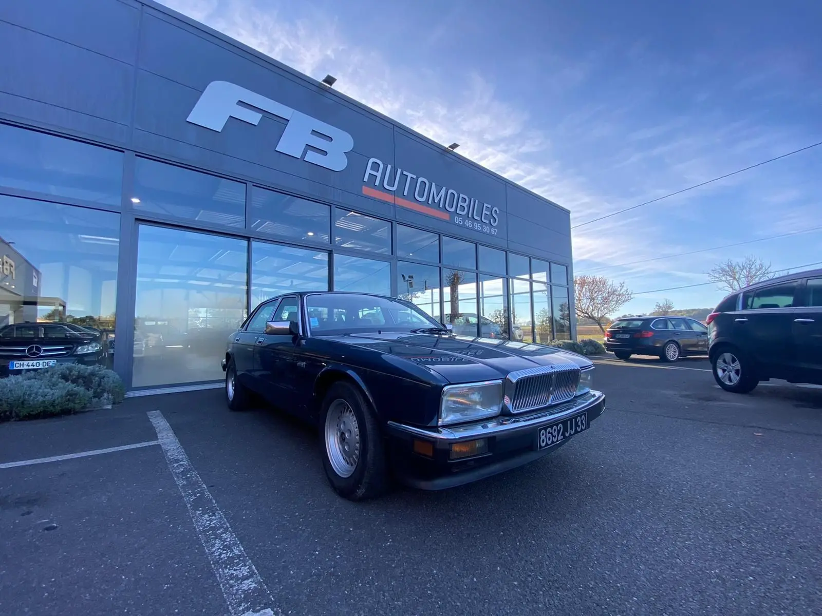 Jaguar XJ6 3.6 Sovereign bleu vue 3/4 avant droit devant concession FB Automobiles par temps clair.