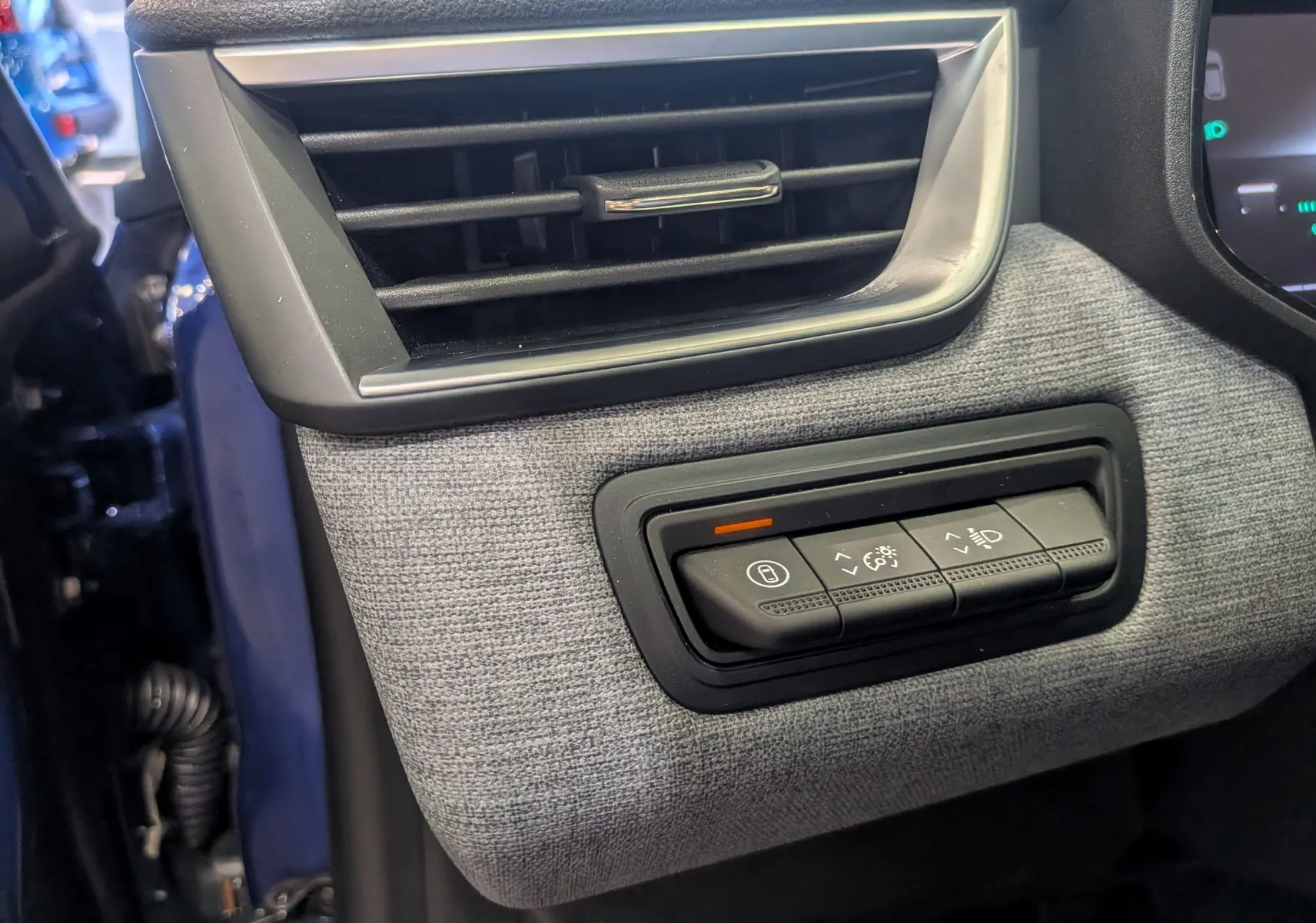 Détail intérieur côté gauche montrant la commande d’éclairage et la ventilation, avec la carrosserie Bleu Iron visible en arrière-plan.