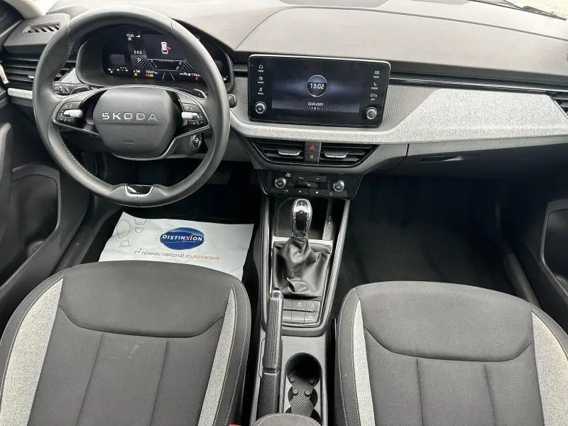 Vue intérieure avant de la Skoda Scala 2025, tableau de bord avec écran tactile, volant cuir multifonction et sièges tissu noir/gris.