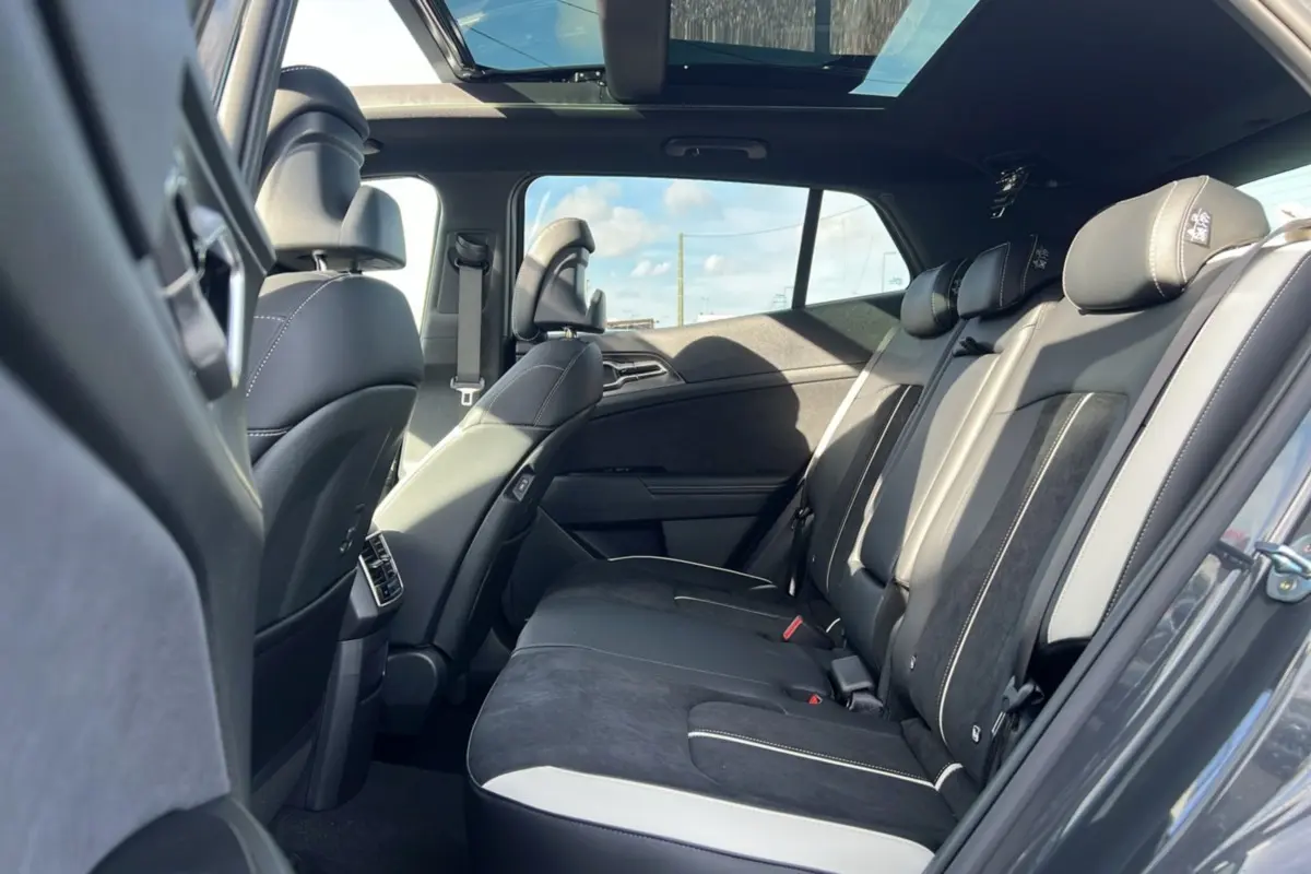 Vue intérieure arrière droite du Kia Sportage 2026 gris eclipse avec toit panoramique et sièges en cuir noir et alcantara.