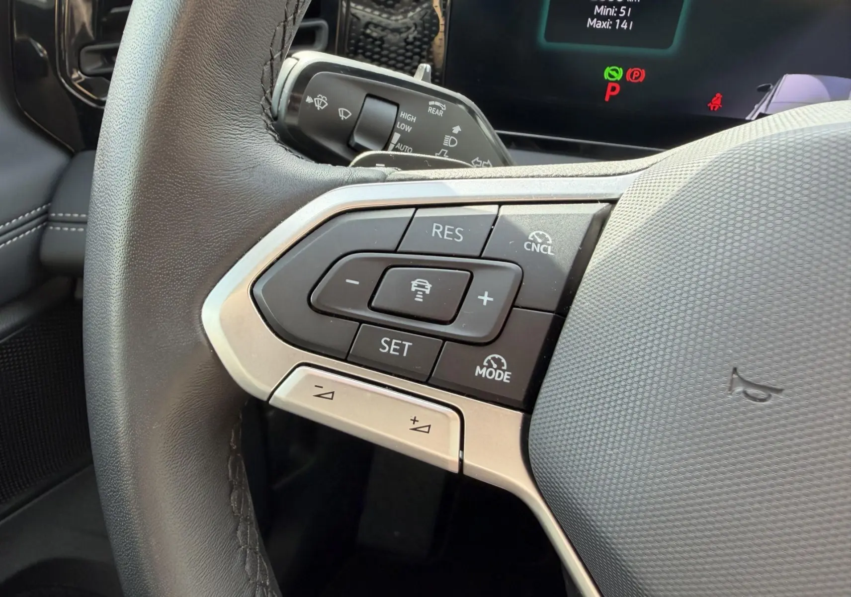 Gros plan sur les commandes du volant cuir noir du Volkswagen Tiguan 2025, avec affichage digital en arrière-plan.
