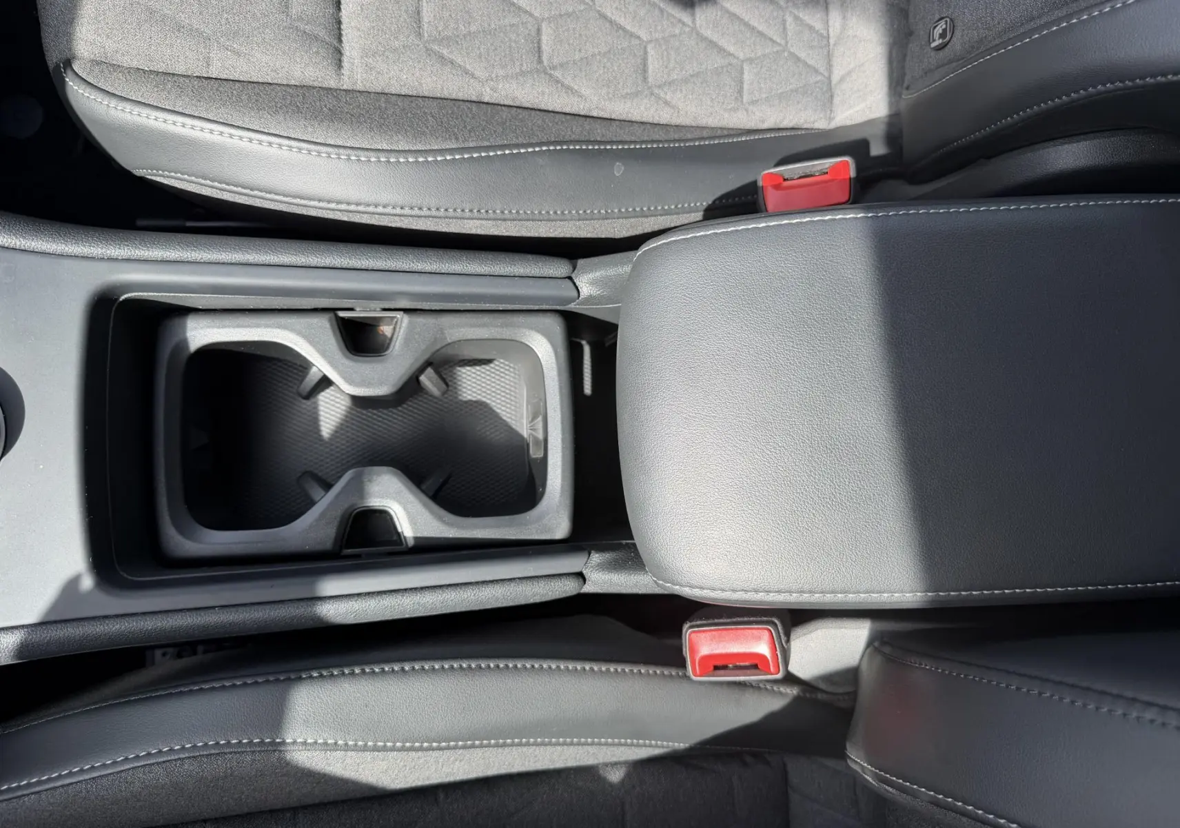 Vue plongeante sur la console centrale noire du Volkswagen Tiguan 2025, avec porte-gobelets et accoudoir en cuir.