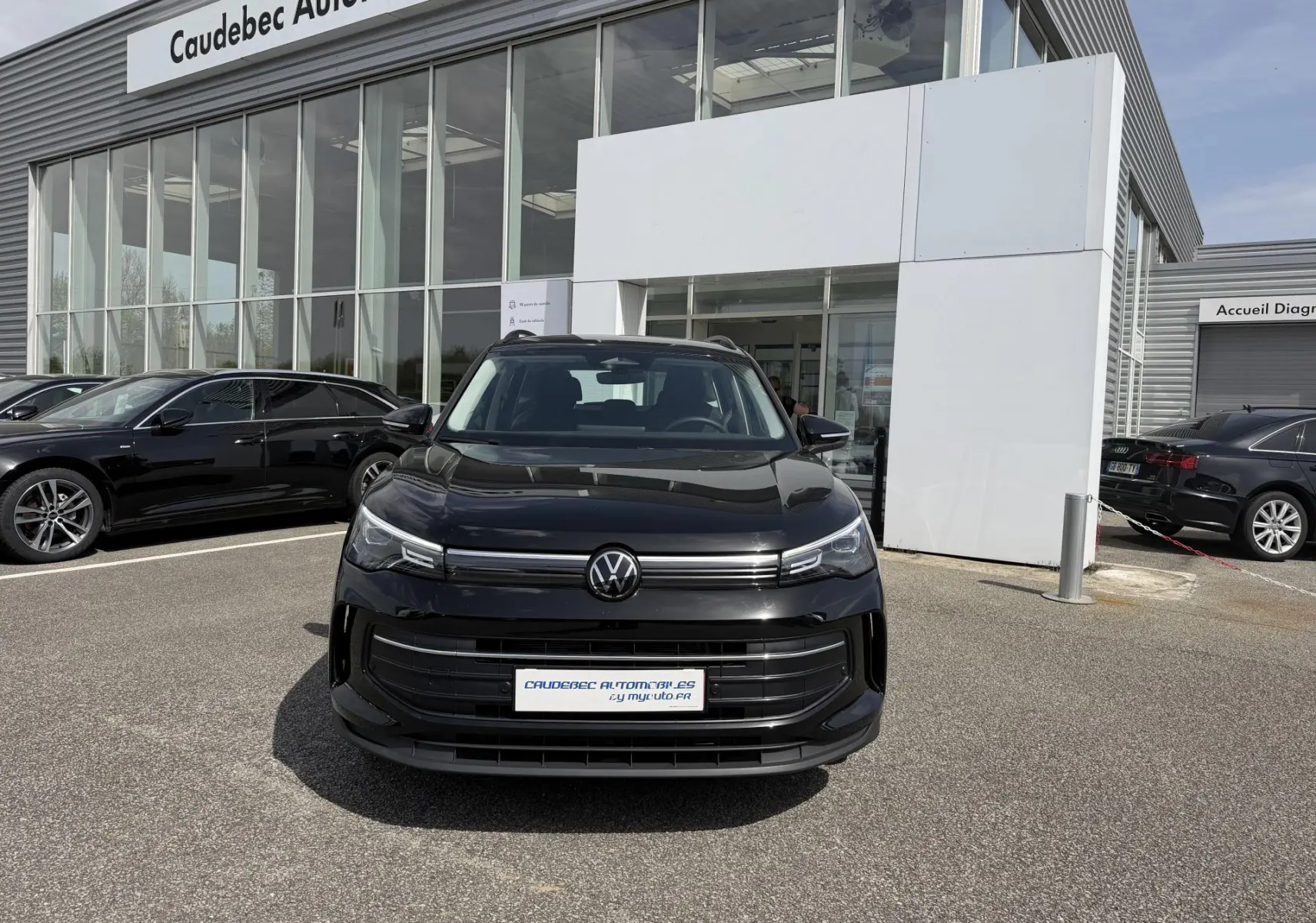 Volkswagen Tiguan noir vue de face, stationné devant un showroom avec calandre moderne et phares LED fins.