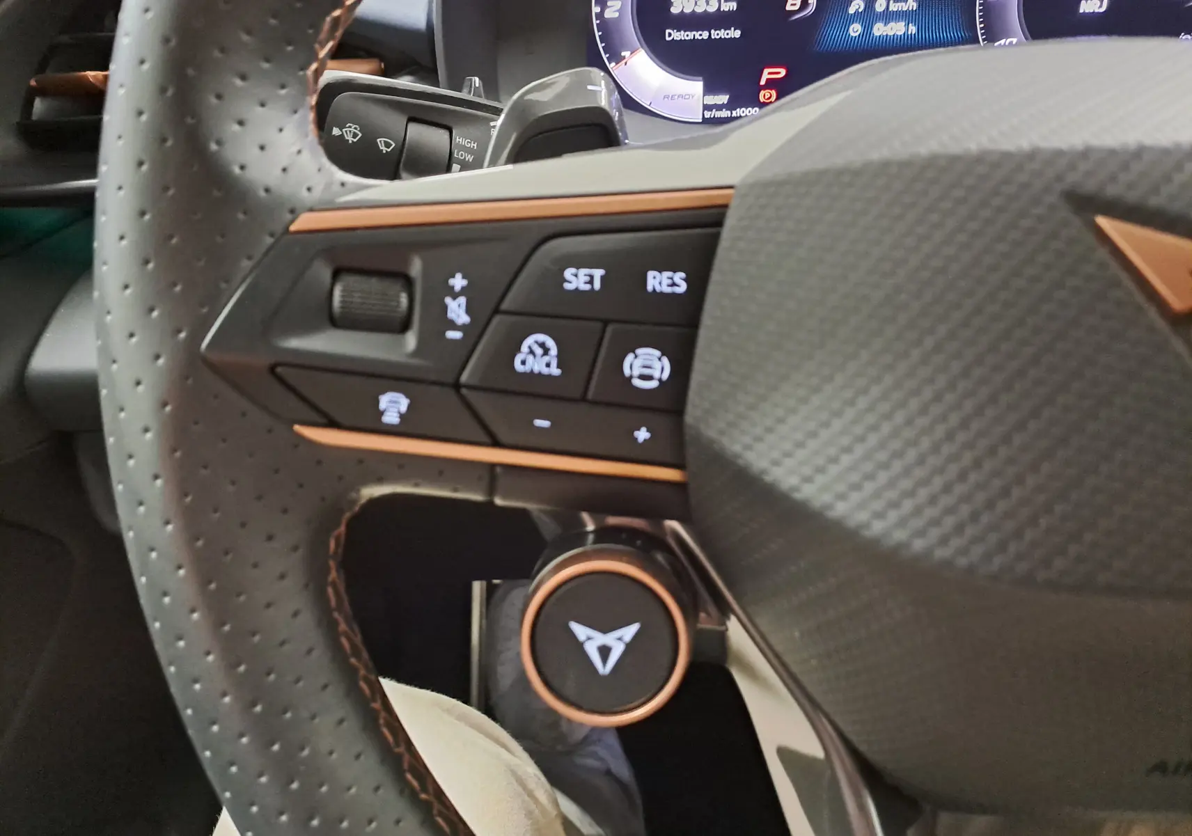 Gros plan sur le volant perforé du CUPRA Terramar 2025 avec commandes intégrées et logo cuivre au centre.