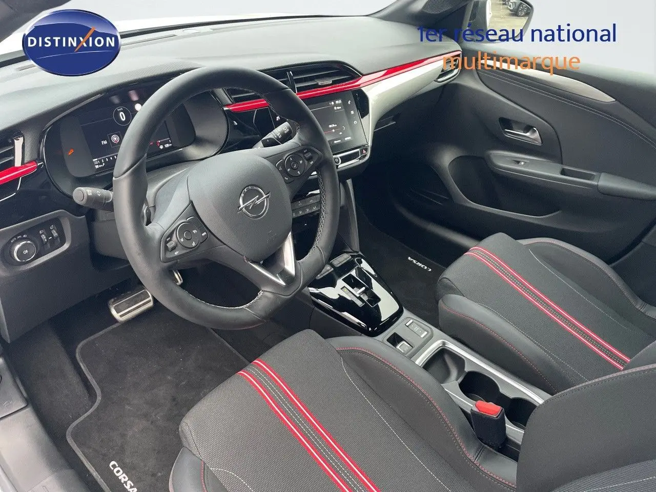 Intérieur avant droit de l'Opel Corsa blanc 2022, avec volant multifonction et sièges noirs à surpiqûres rouges.