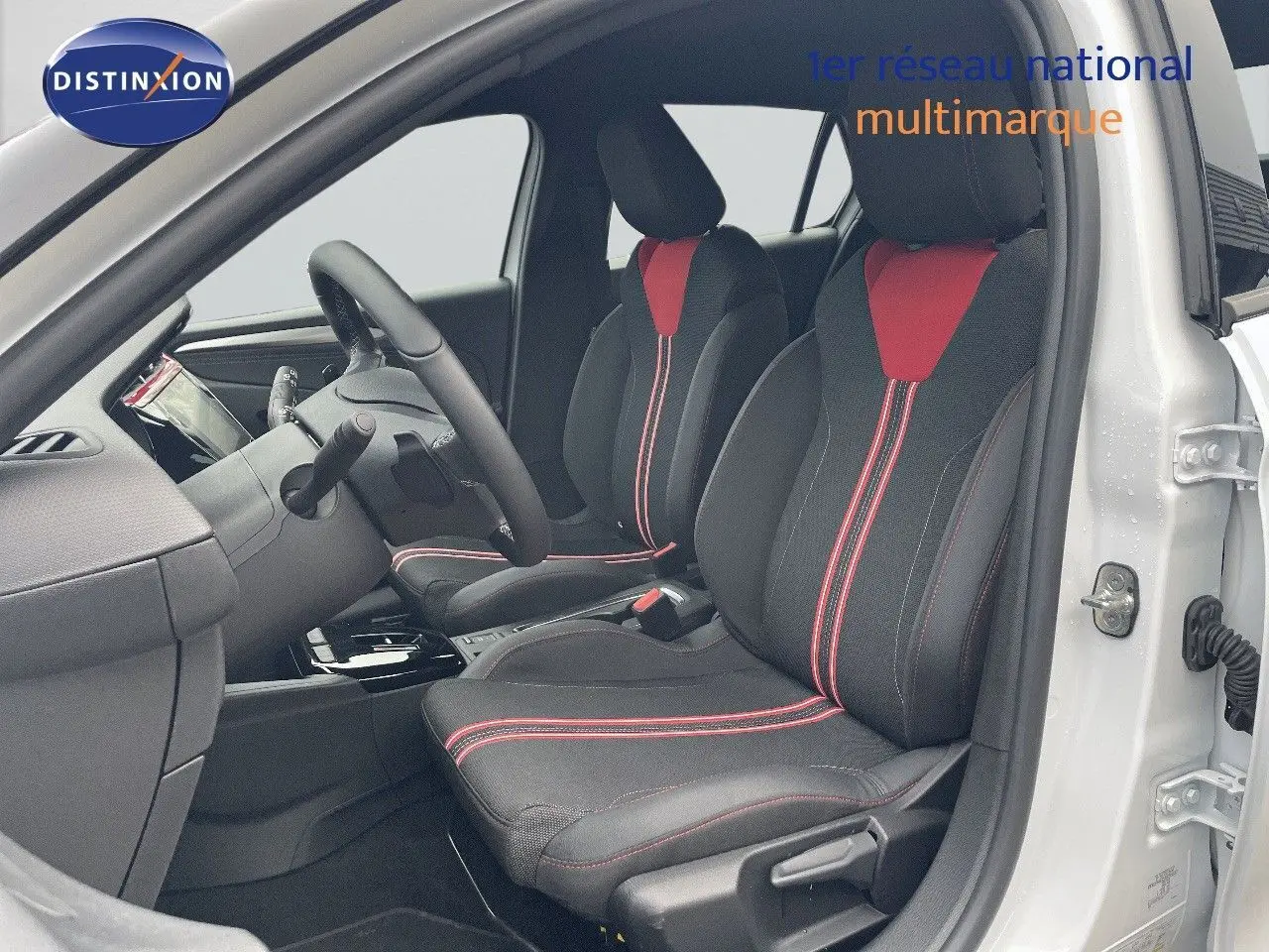 Vue intérieure côté conducteur d'une Opel Corsa blanche 2022 avec sièges noirs et rouges à surpiqûres rouges.