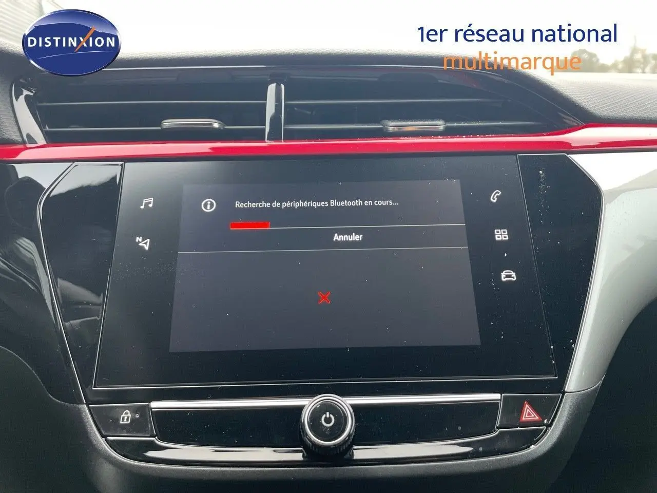 Écran tactile central de la console d'une Opel Corsa blanche, avec une barre rouge décorative au-dessus.