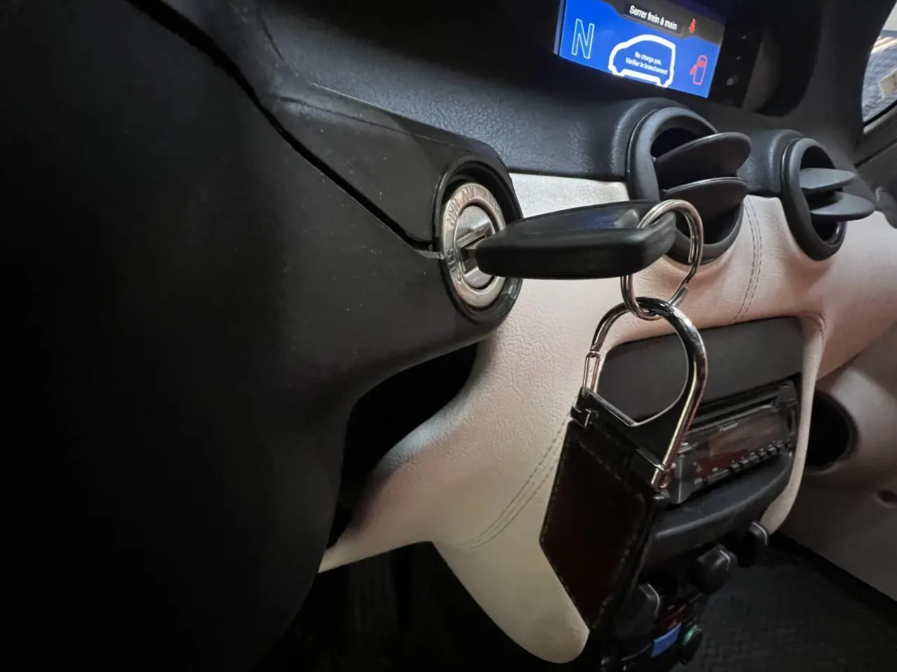 Gros plan intérieur sur le tableau de bord beige et noir du Citroën E-MEHARI cabriolet bleu clair avec clé insérée dans le contacteur.