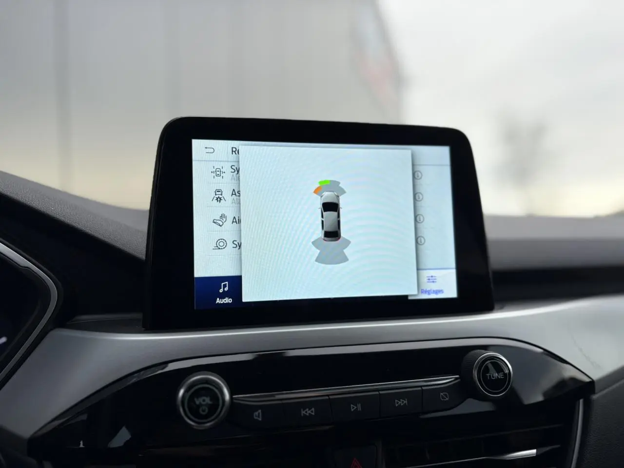 Écran tactile central du Ford Kuga 2024 affichant l'aide au stationnement avec vue de dessus du véhicule.