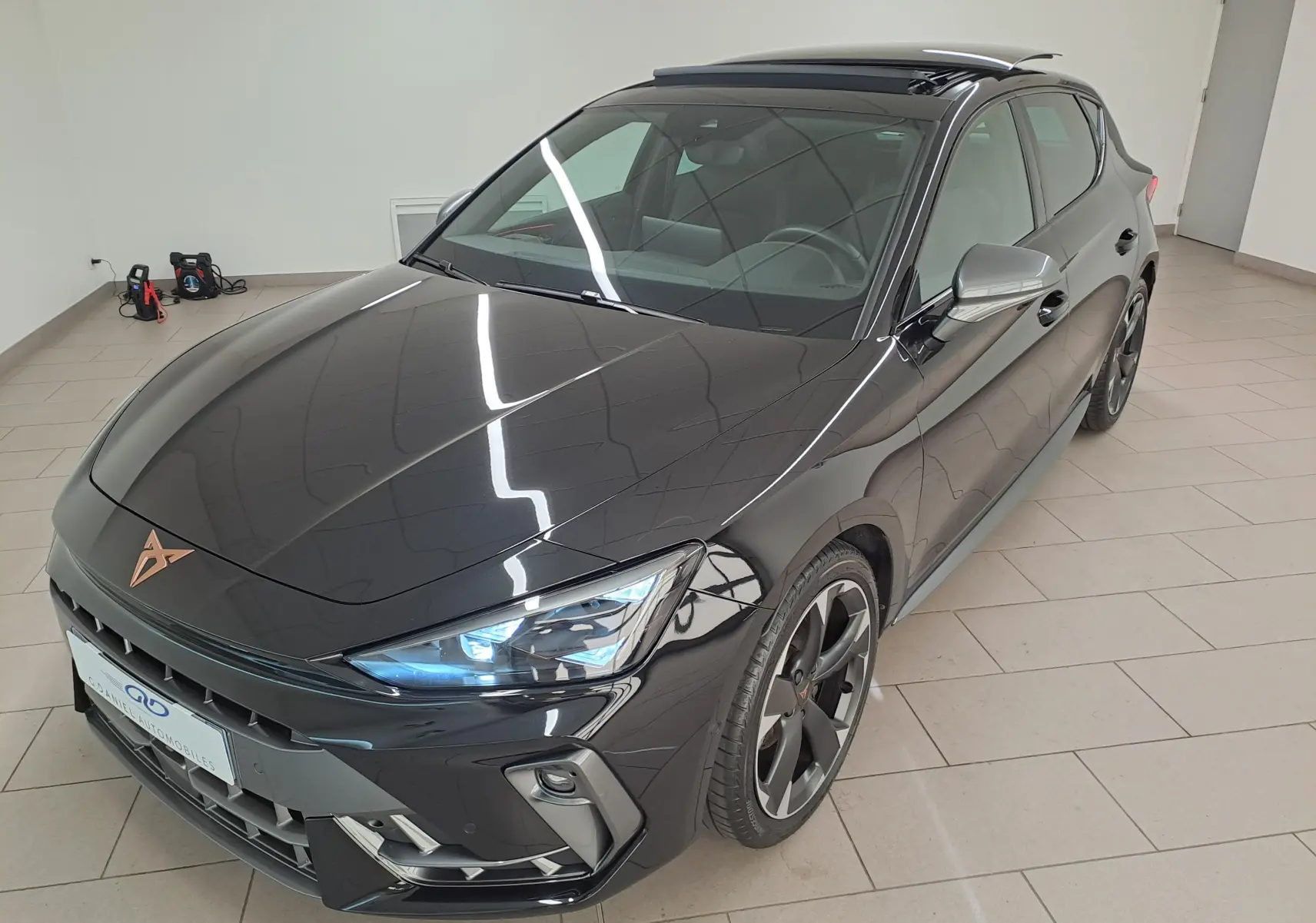 Vue 3/4 avant droite d'une CUPRA Leon 2025 Noir Minuit avec toit ouvrant panoramique et projecteurs Matrix LED allumés.