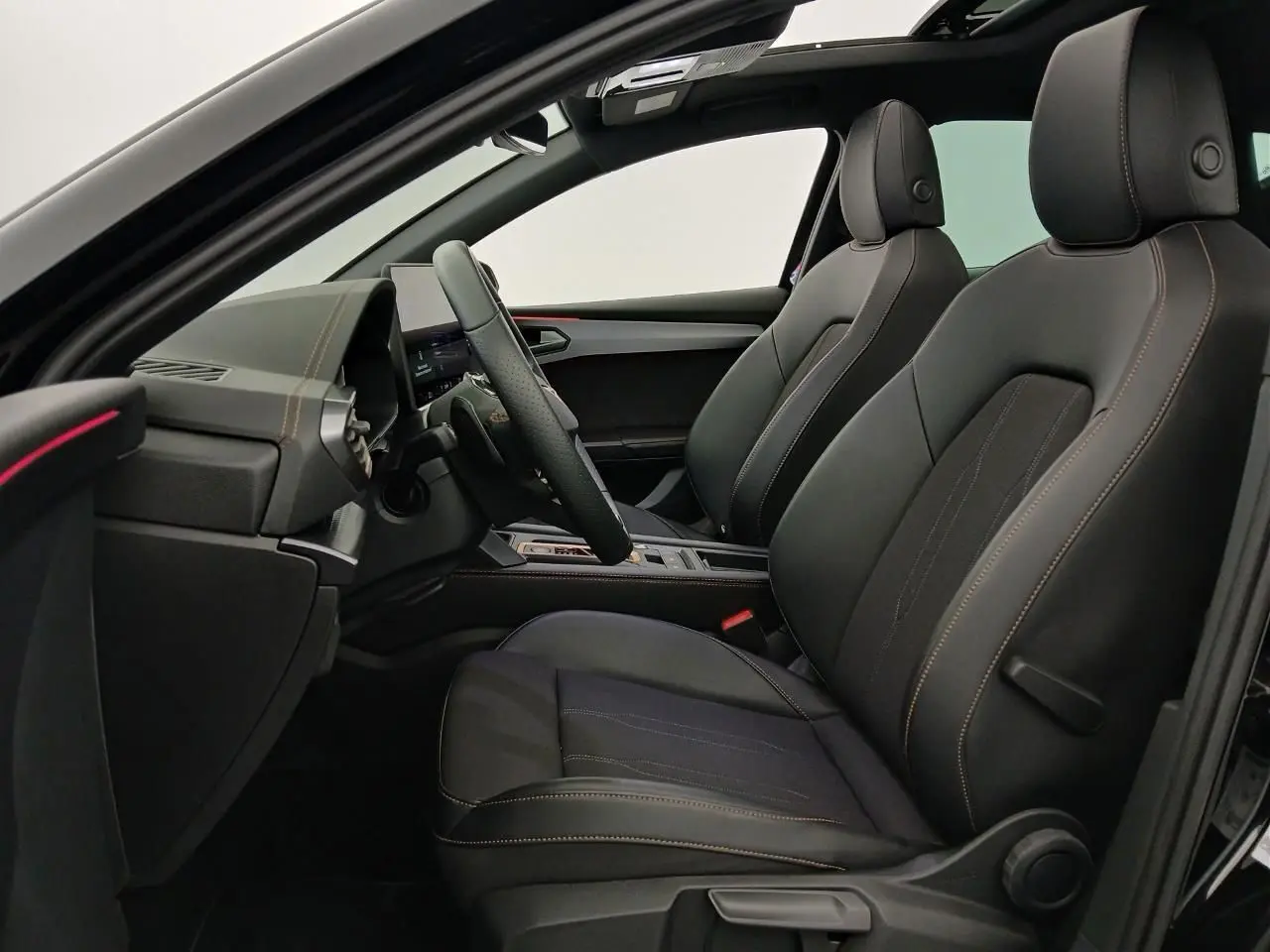 Vue intérieure côté conducteur de la CUPRA Leon 2025 avec sièges noirs, coutures contrastées et toit ouvrant panoramique.