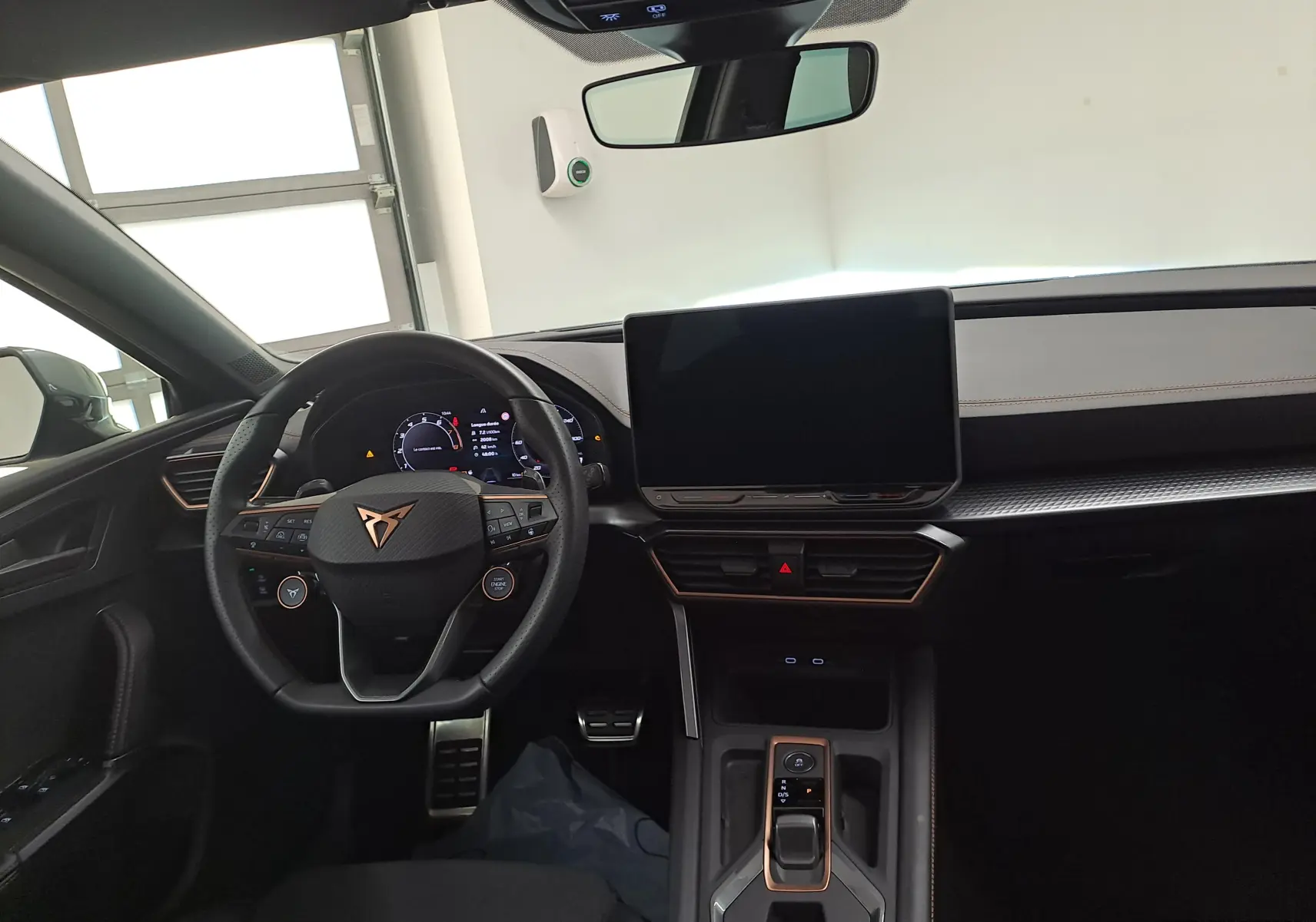 Vue intérieure avant du tableau de bord du CUPRA Leon 2025, avec volant multifonction et écran tactile central.