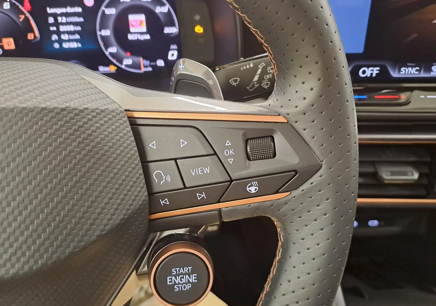 Gros plan sur le volant côté droit de la CUPRA Leon 2025, avec boutons multifonctions et démarreur intégré, ambiance intérieure noire et cuivre.