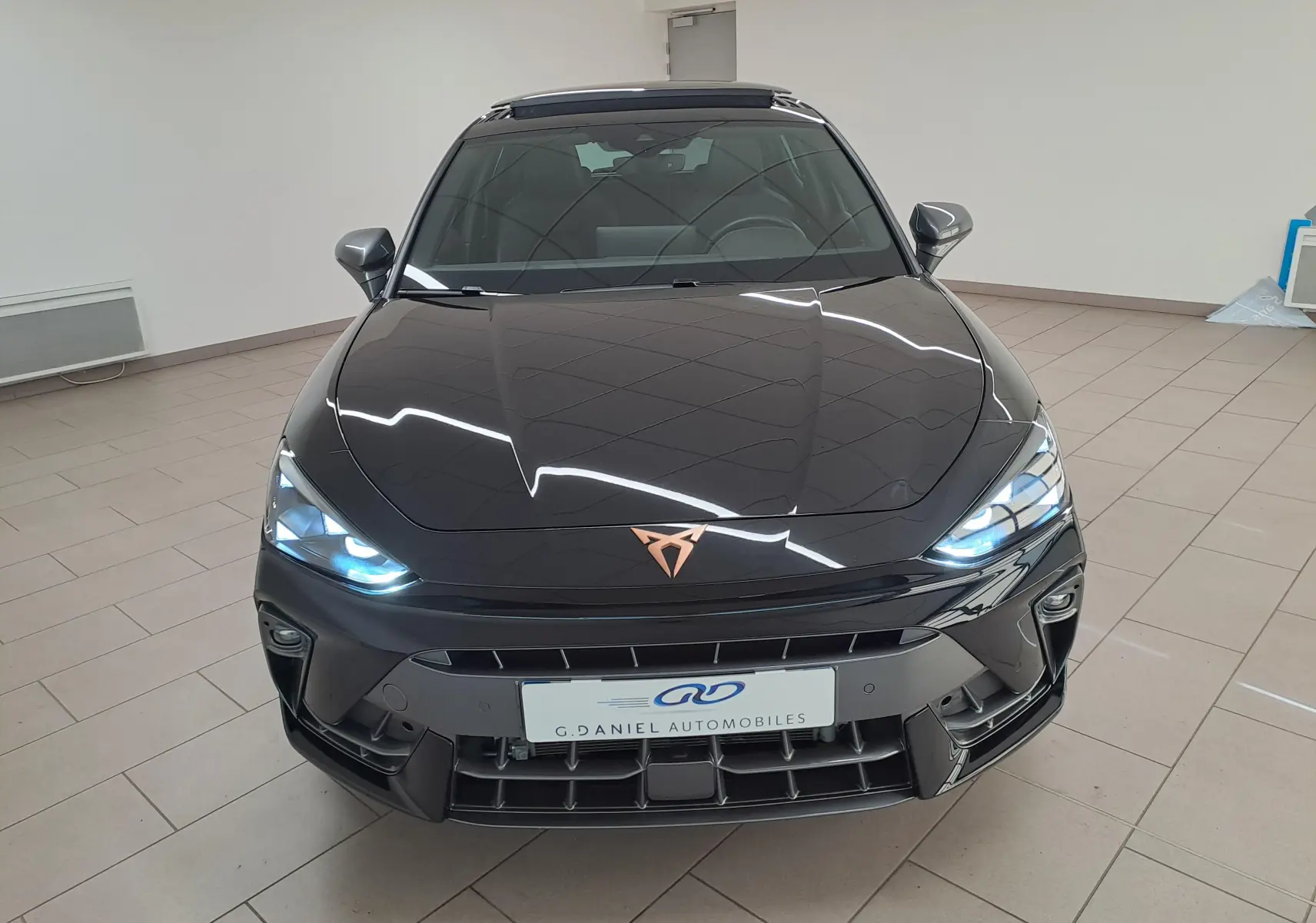 Vue avant d'une CUPRA Leon 2025 noir minuit avec projecteurs Matrix LED allumés et toit ouvrant panoramique visible.