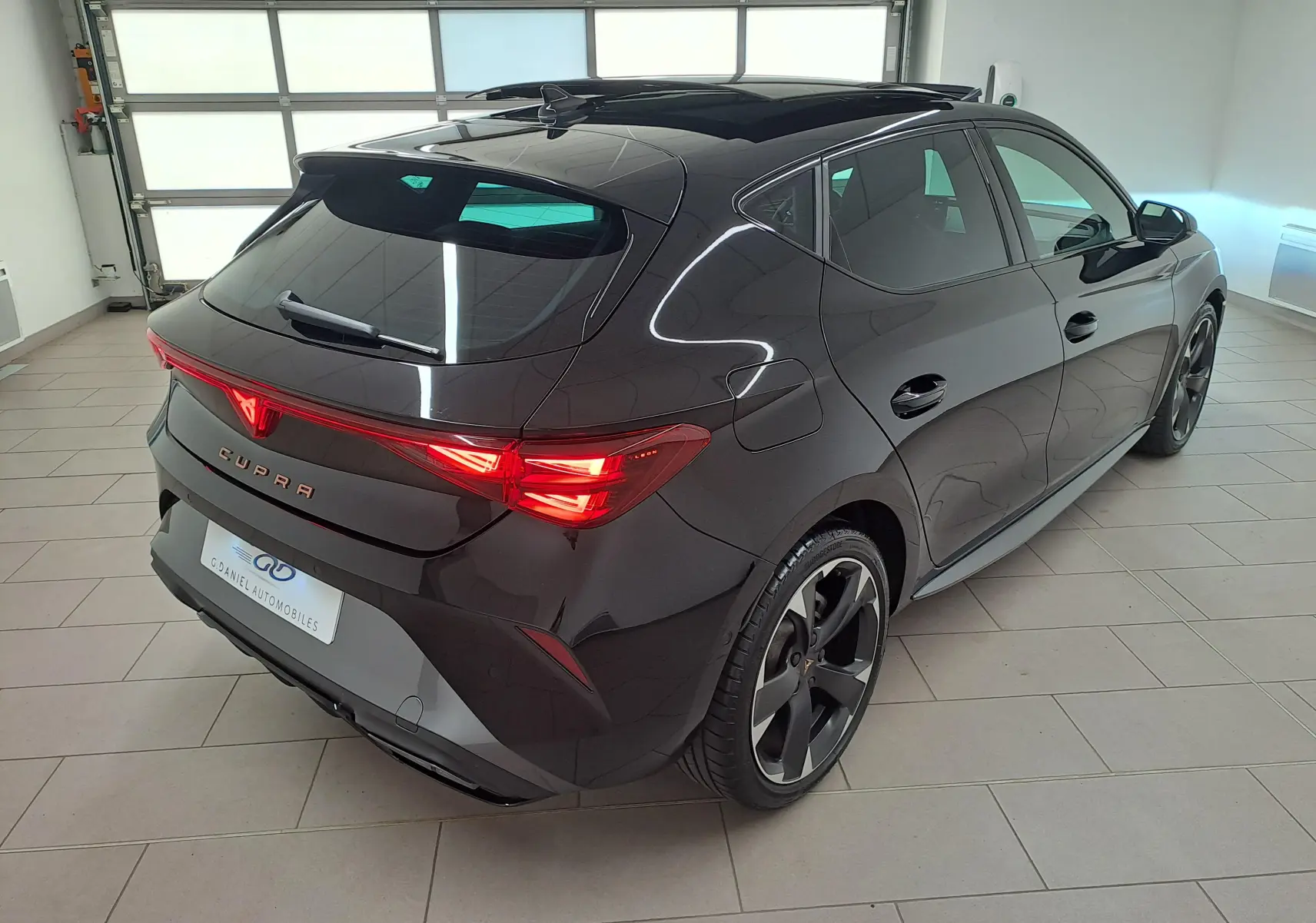 Vue 3/4 arrière droite d'une CUPRA Leon Noir Minuit avec toit ouvrant panoramique et feux arrière Matrix LED allumés.