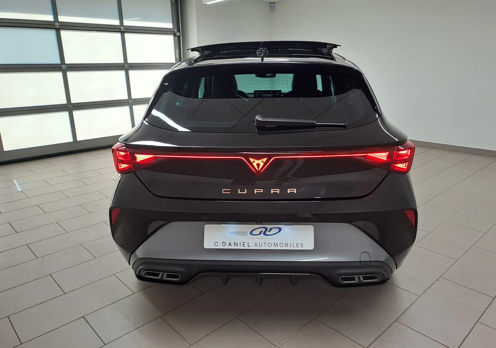 Vue arrière d'une CUPRA Leon 2025 Noir Minuit avec feux LED allumés et double sortie d'échappement intégrée.