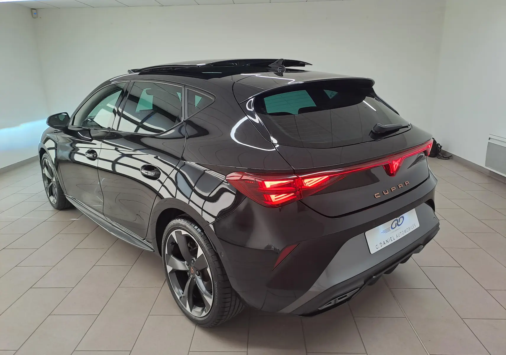 Vue 3/4 arrière droite d'une CUPRA Leon 2025 noir minuit avec toit ouvrant panoramique et feux arrière LED allumés.