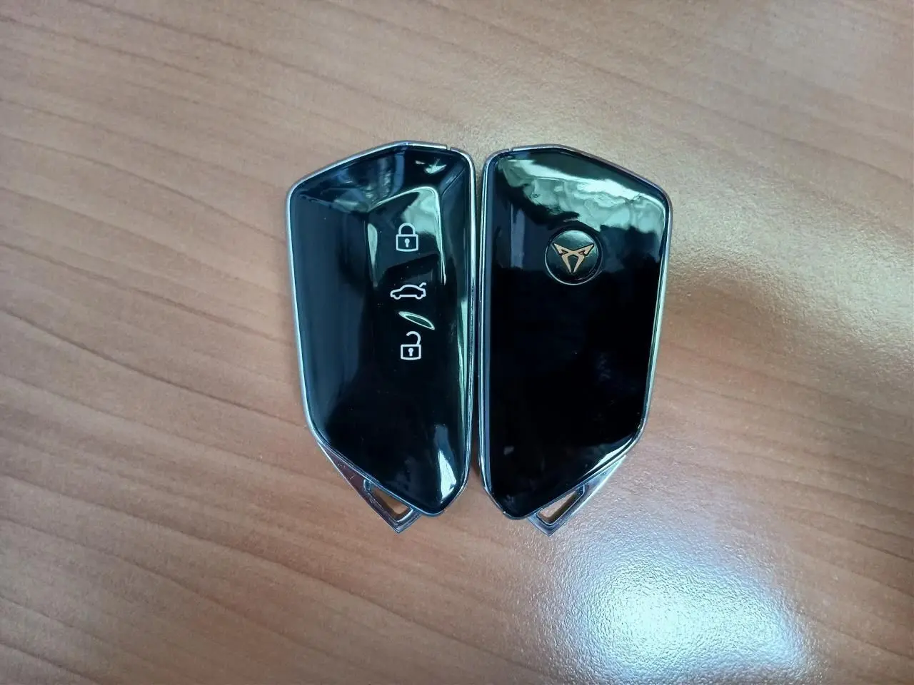 Clé de voiture CUPRA noire brillante avec logo doré, vue rapprochée sur fond bois clair.