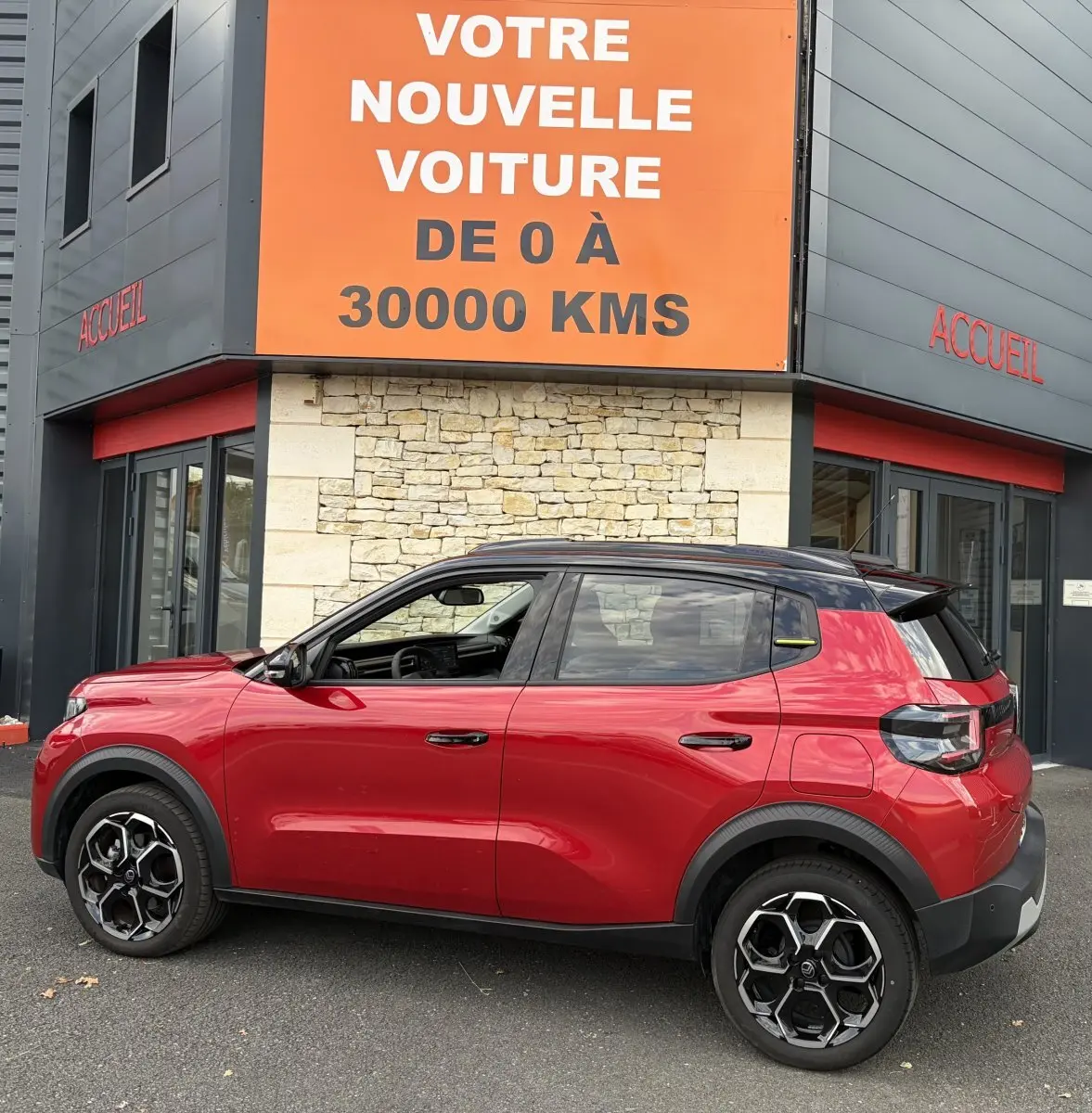 Vue de profil droit d'une Citroën C3 Turbo 100 BVM6 MAX rouge avec toit noir et jantes distinctives, devant un bâtiment.