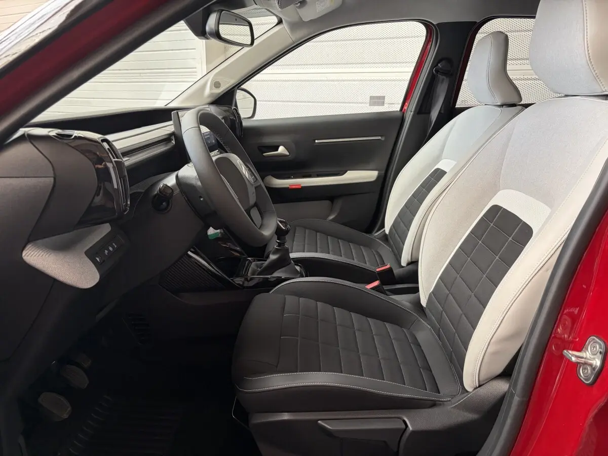Vue intérieure côté conducteur d'une Citroën C3 rouge 2025, sièges bi-ton noir et beige, volant cuir et tableau de bord moderne.