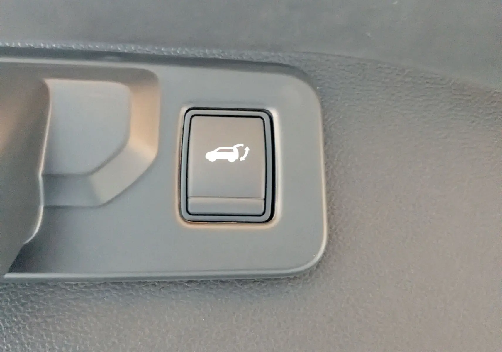 Bouton intérieur noir avec symbole blanc d'ouverture du hayon, situé sur la garniture du coffre du Renault Austral E-Tech.