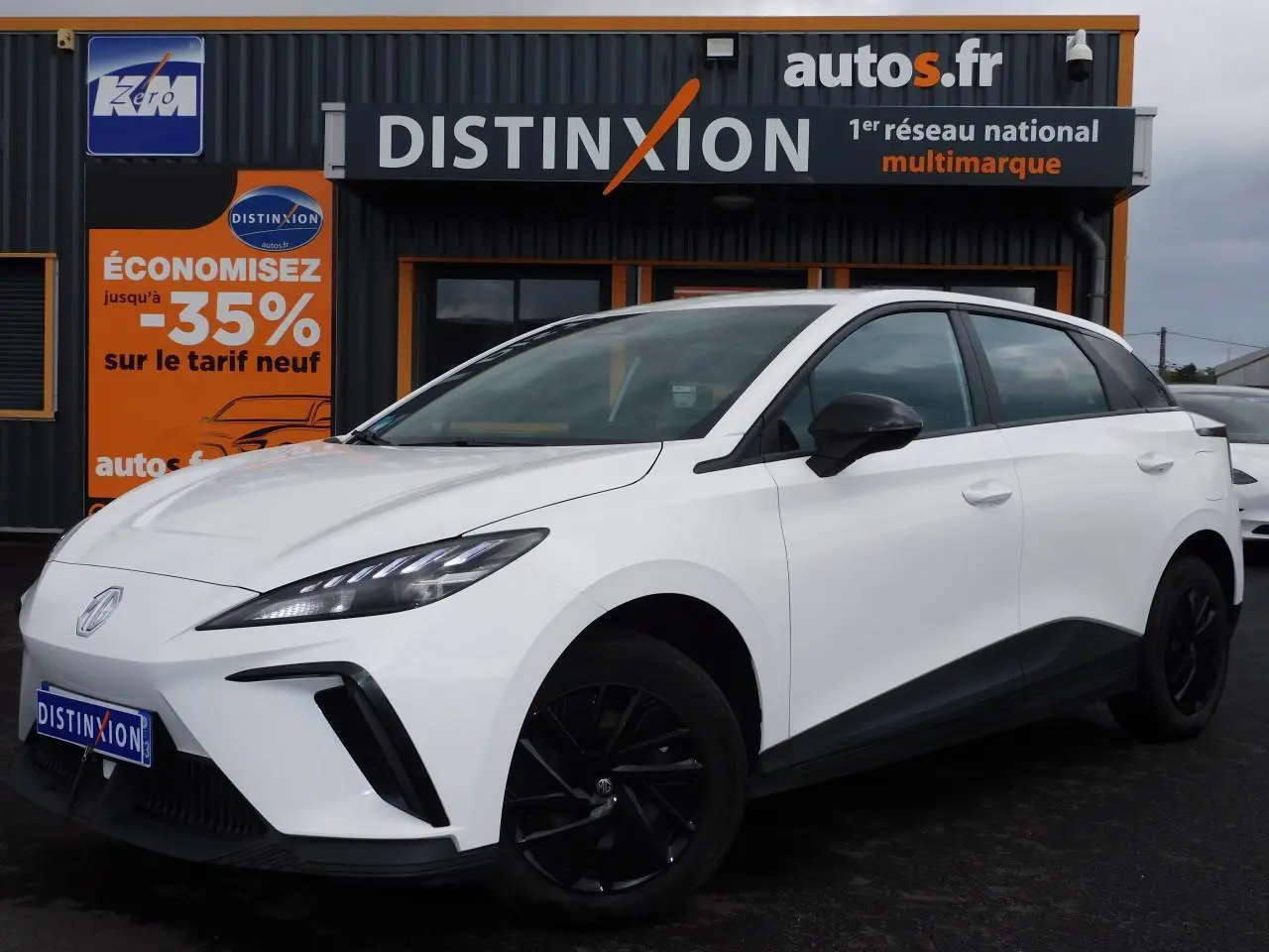 MG4 blanc en vue 3/4 avant droit, avec jantes noires et lignes épurées sous un ciel nuageux.