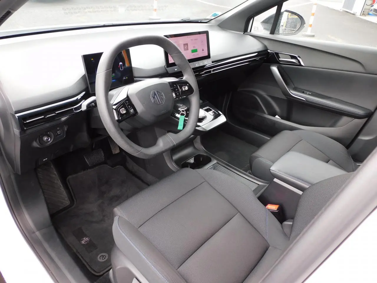 Intérieur noir du MG4 2023 vu côté conducteur, avec volant simili-cuir et écran tactile central lumineux.