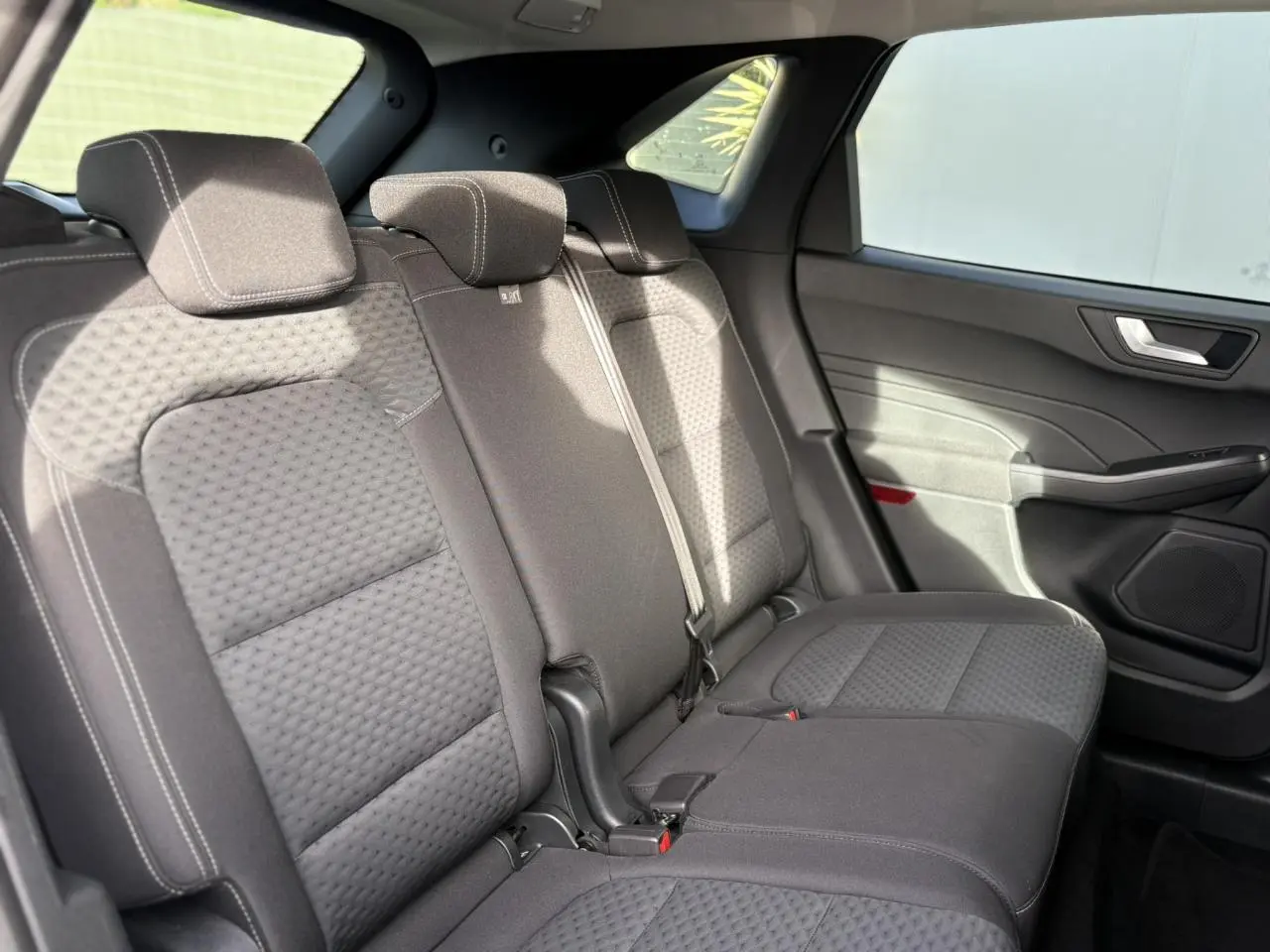 Vue intérieure côté droit des sièges arrière en tissu gris du Ford Kuga 2024, avec ceinture de sécurité et porte.