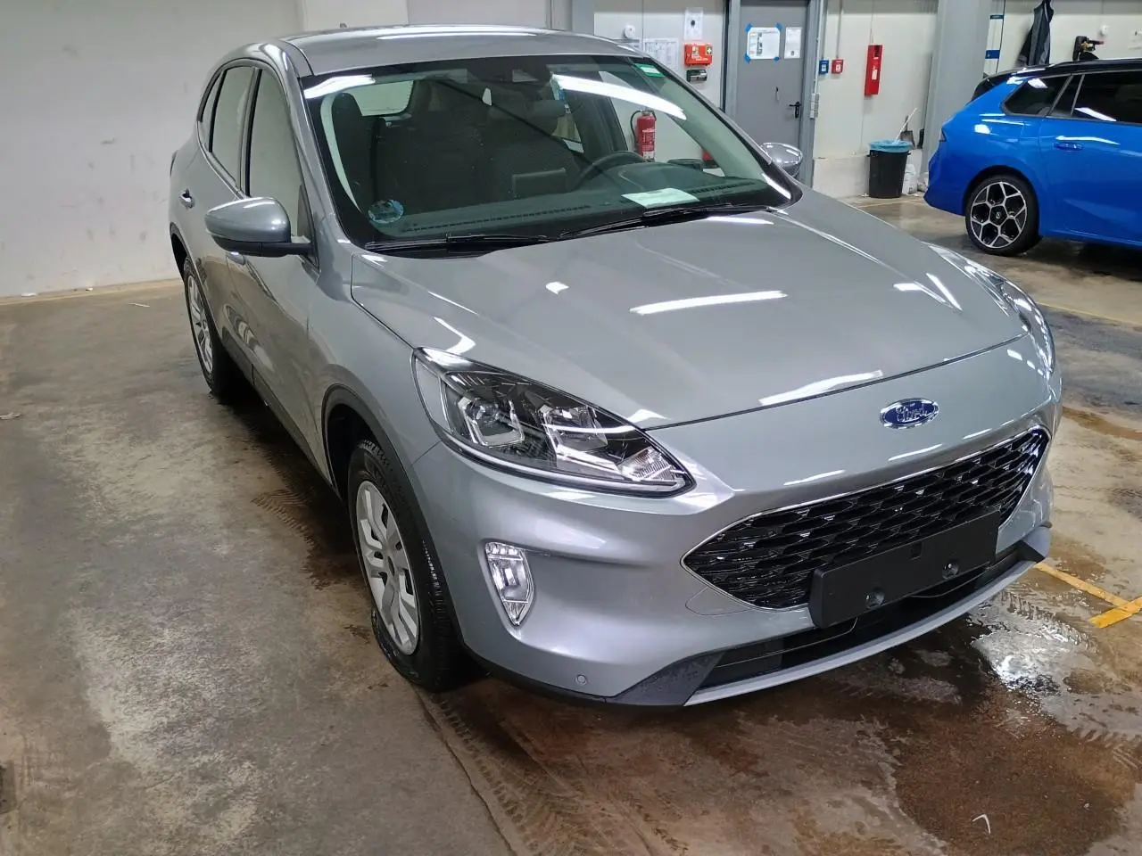 Ford Kuga gris Solar vu en 3/4 avant droit dans un garage, avec calandre noire et phares modernes.