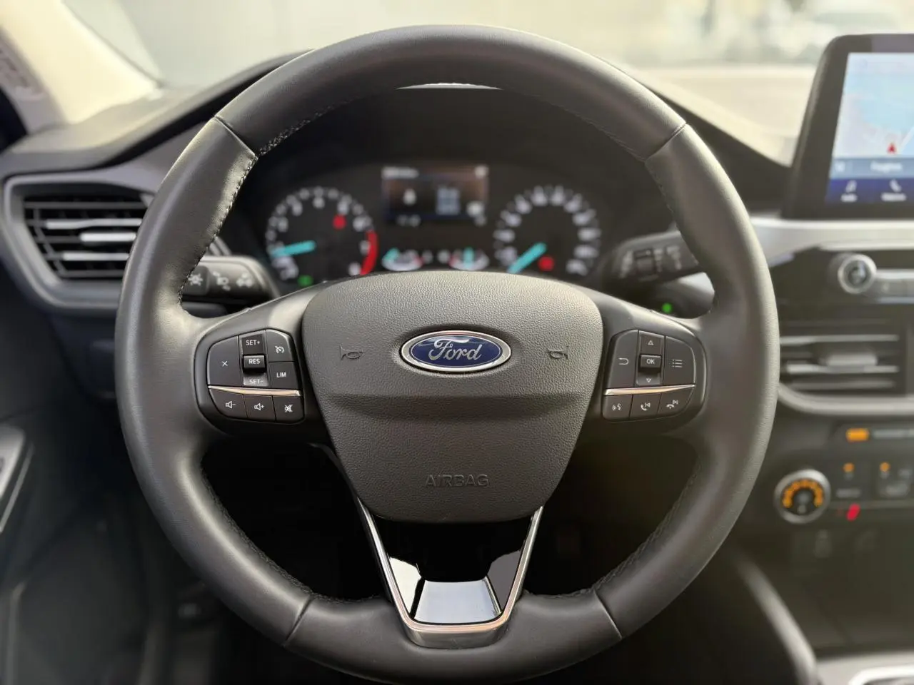 Vue rapprochée du volant en cuir noir du Ford Kuga 2024 avec commandes multifonctions et tableau de bord flou en arrière-plan.