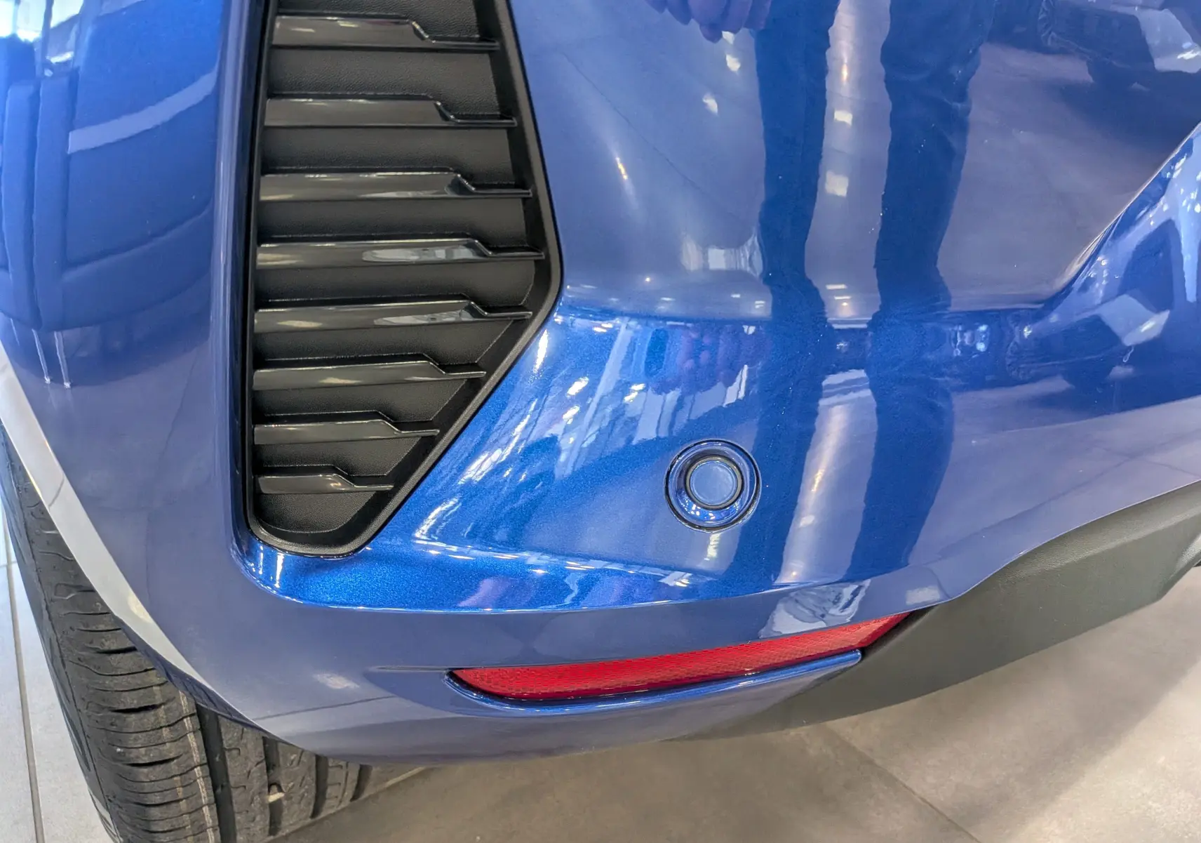 Détail du pare-chocs arrière bleu Iron de la Renault Clio V avec capteur de recul et feu réfléchissant rouge.