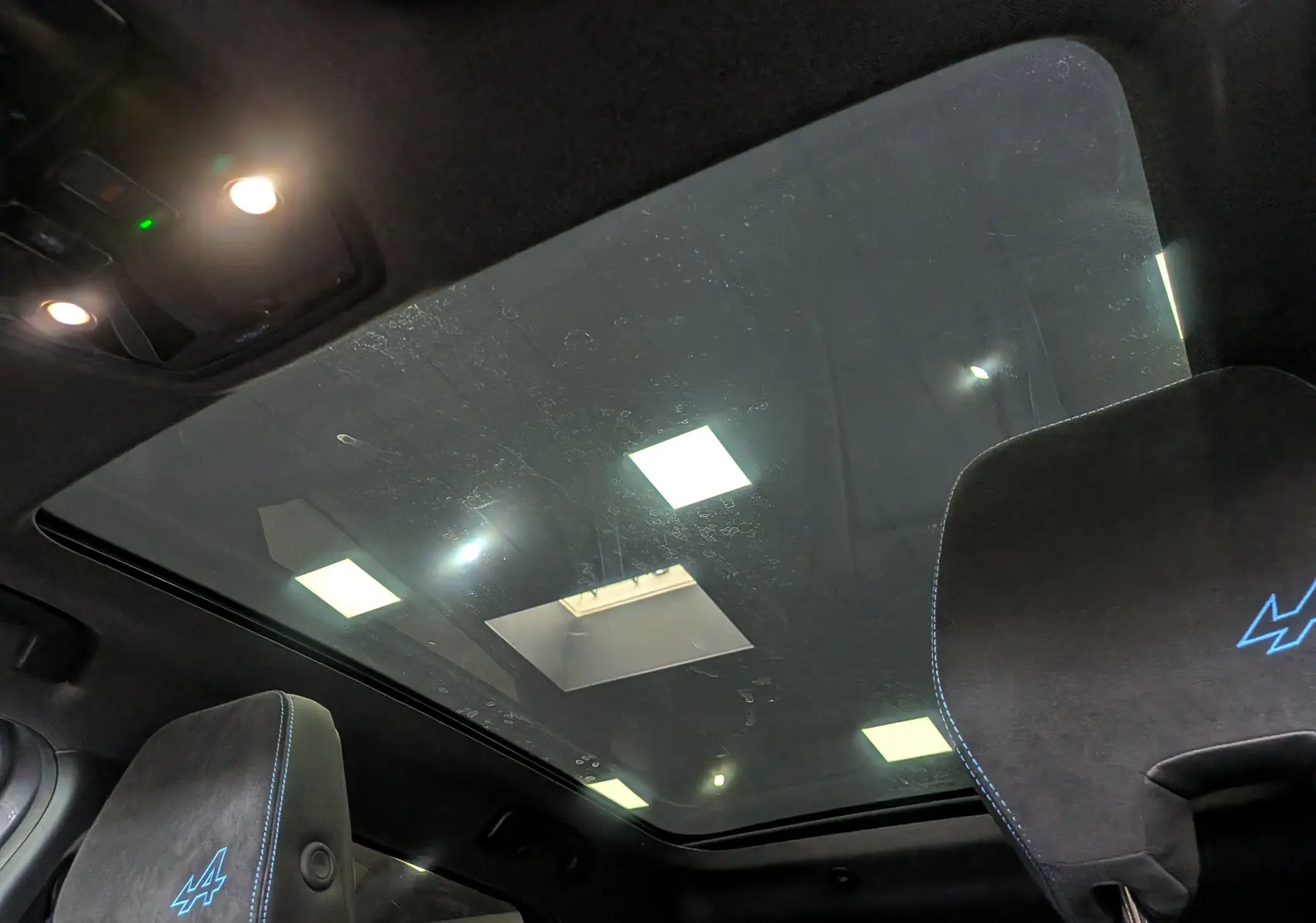 Vue intérieure du toit panoramique du Renault Austral E-Tech hybrid 200 Iconic esprit Alpine avec sièges noirs et logo Alpine bleu.