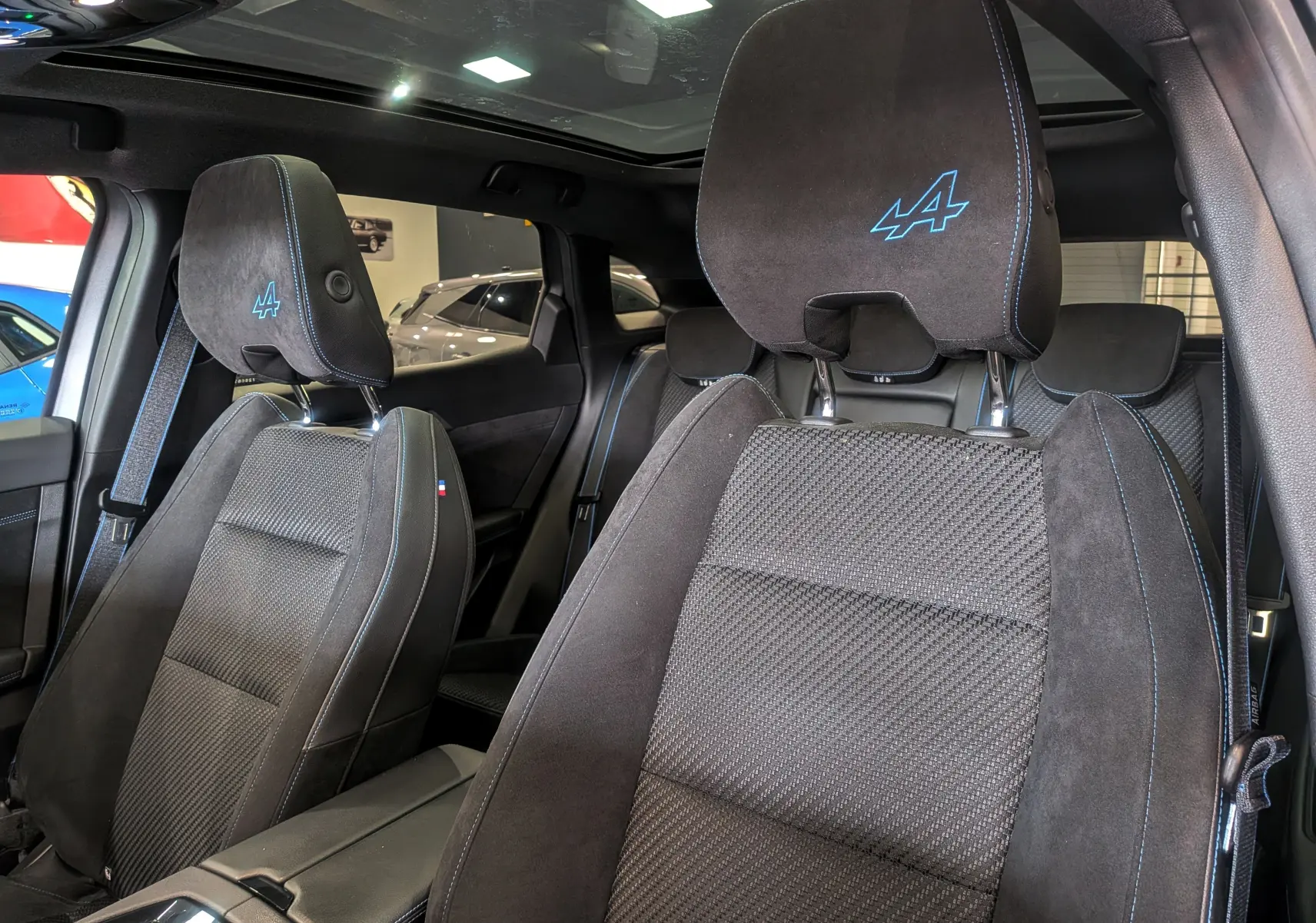 Gros plan sur les sièges avant noirs avec surpiqûres bleues et logo Alpine brodé dans l’habitacle du Renault Austral E-Tech.