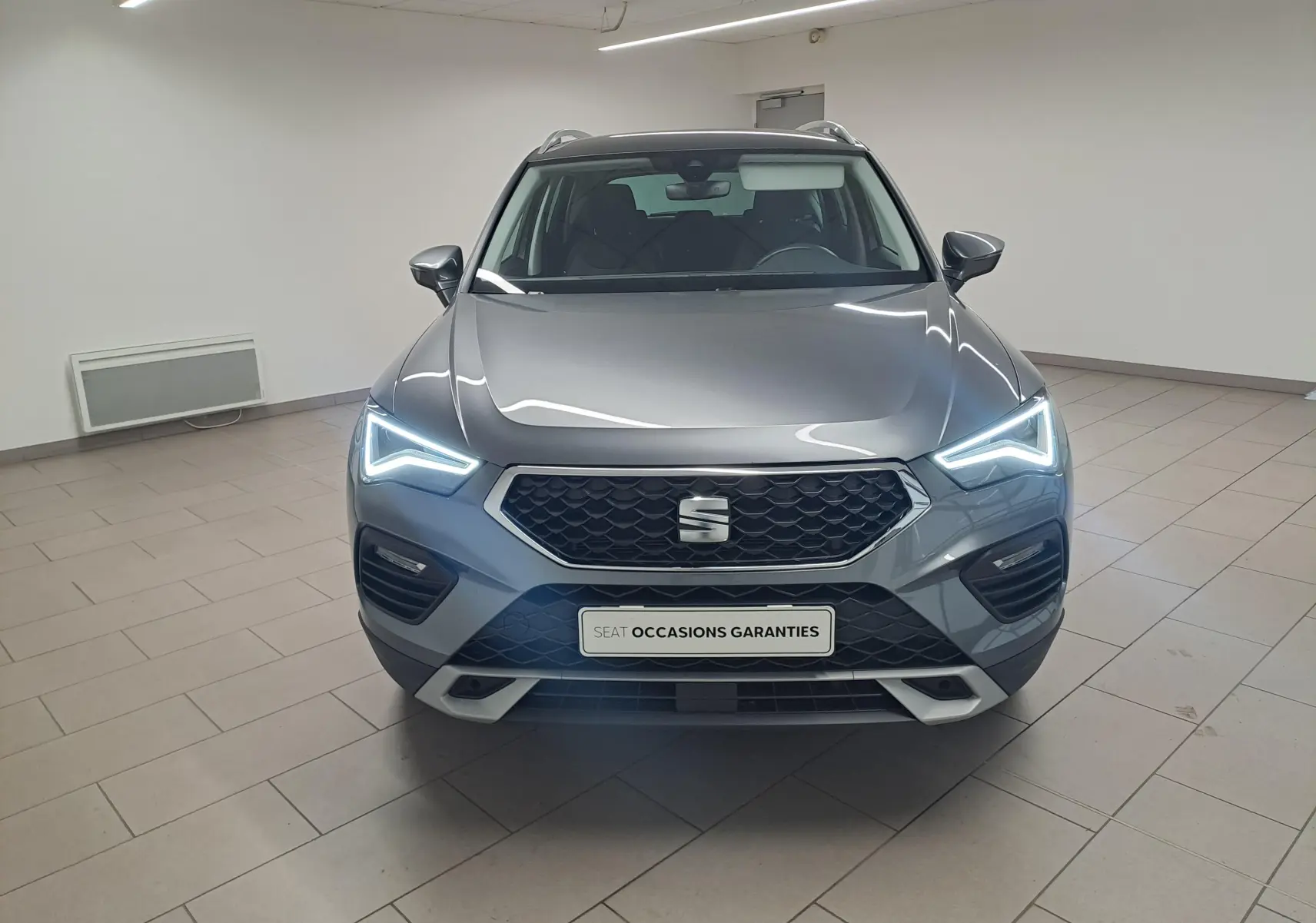 Vue frontale d’un SEAT Ateca gris graphite 2023 avec phares LED allumés dans un showroom intérieur.